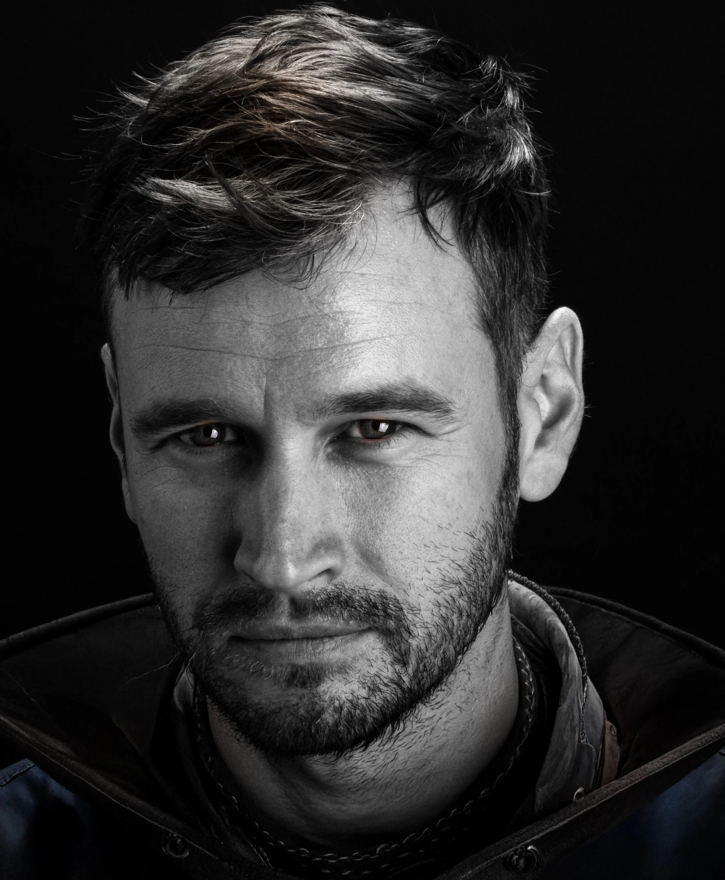 Black-and-white close-up portrait of a bearded man with tousled hair against a dark background
