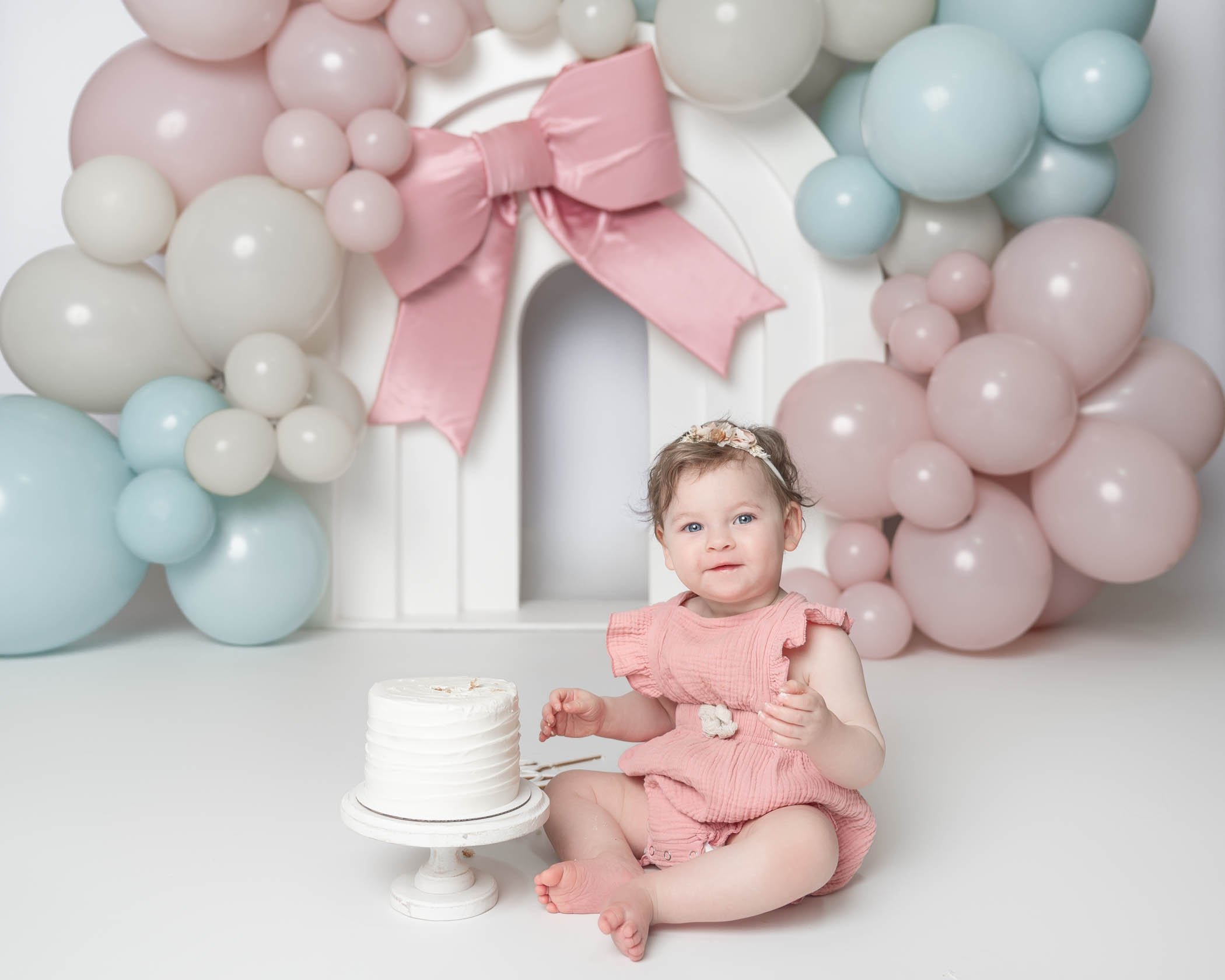 baby girl wearing pink romper during houston cake smash session with pink and blue balloons