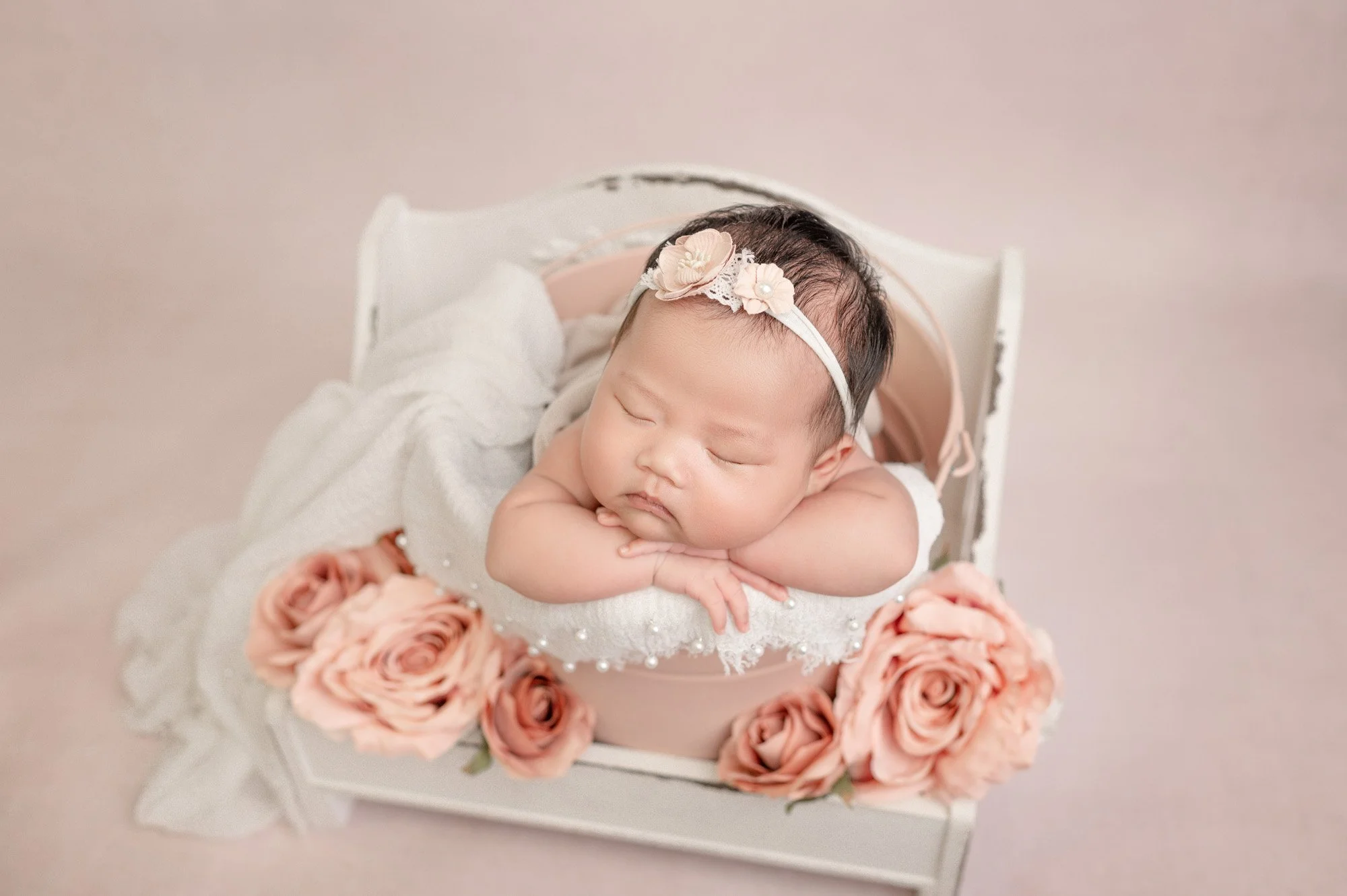 image of newborn baby girl sleeping in bucket surrounded by florals against pink background during houston baby session