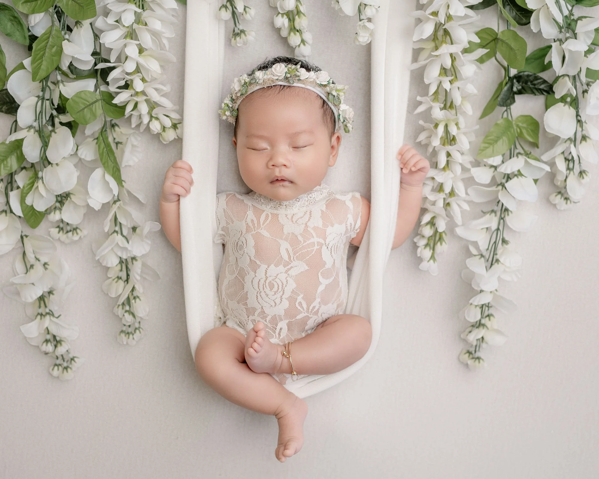 image of newborn baby girl on swing during studio newborn session surrounded by white florals