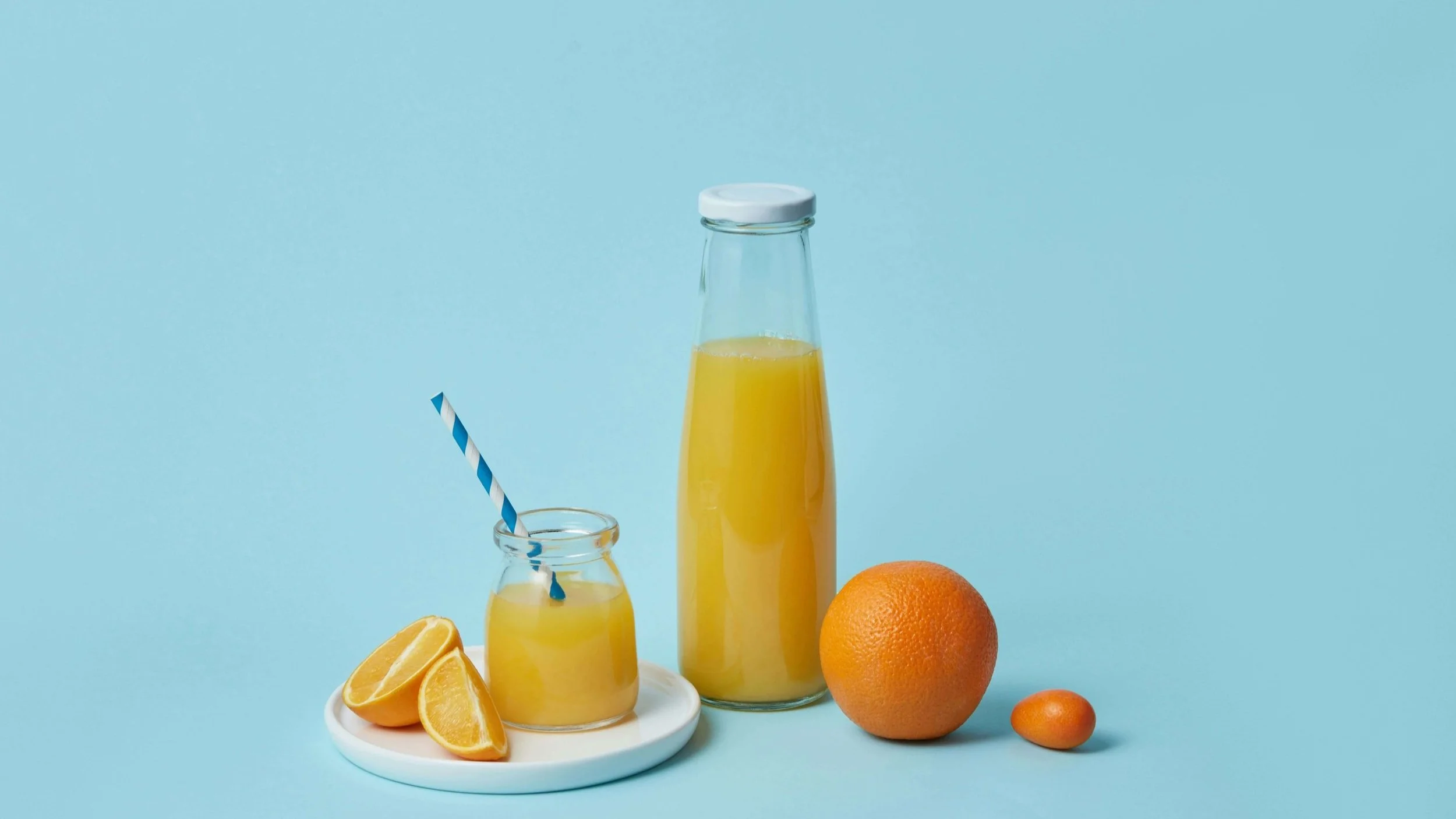 Two bottles of juice with a fresh cut orange and whole fruits
