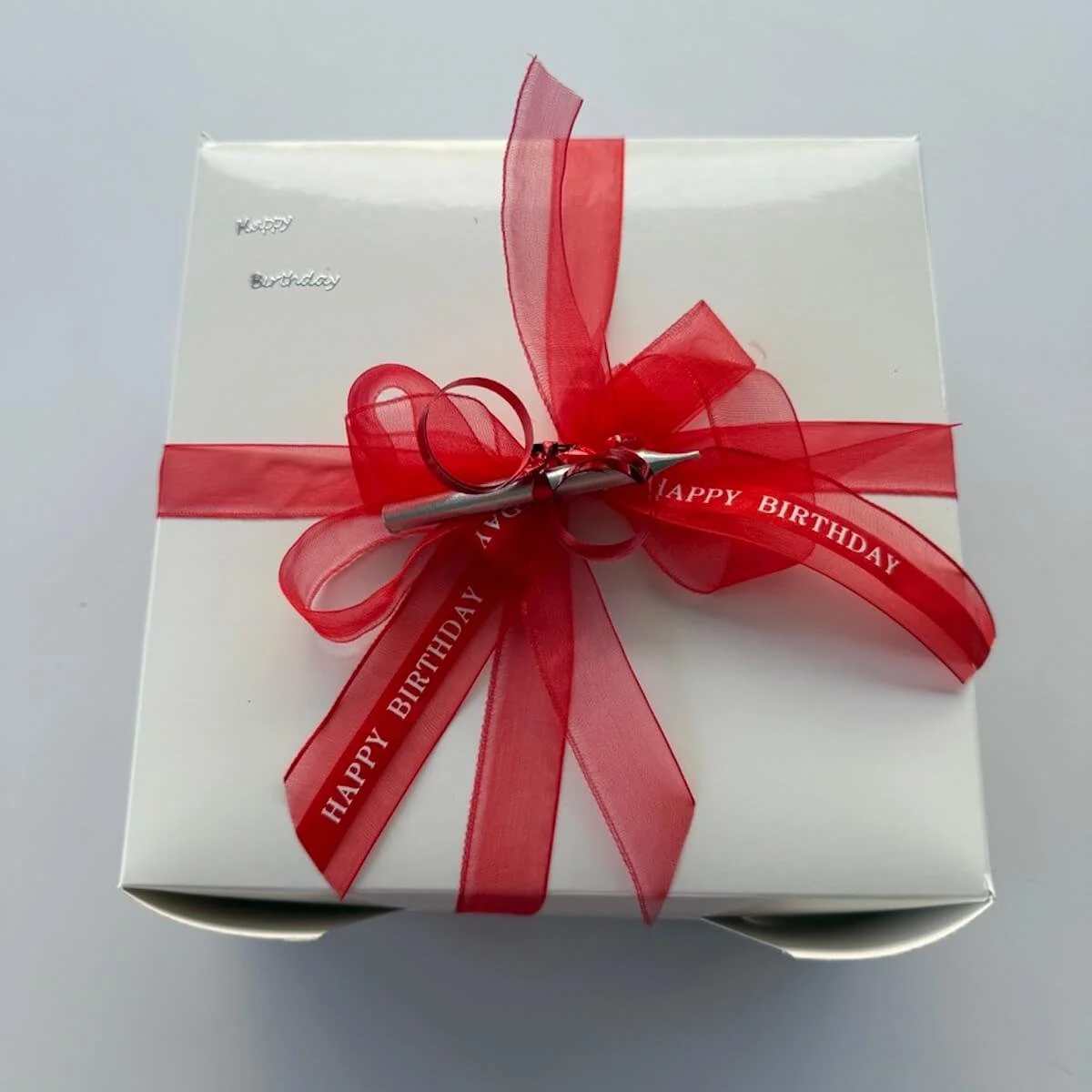 Cake box tied with red ribbon and birthday candle on top.