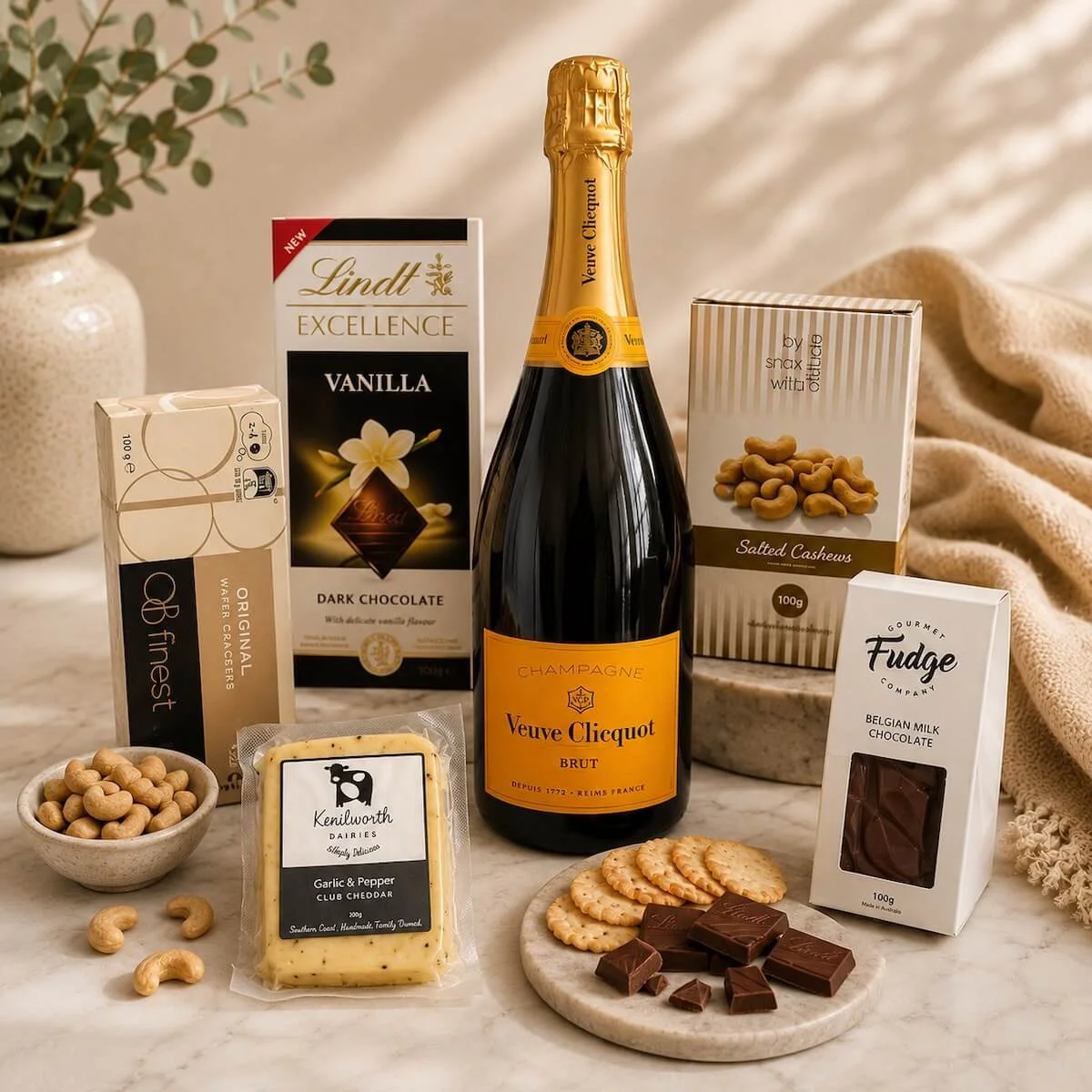 The Veuve for Two gift hamper items displays on a bench Veuve Champagne, Cashews, cheese, crackers, Chocolate and Fudge in a wooden tray.