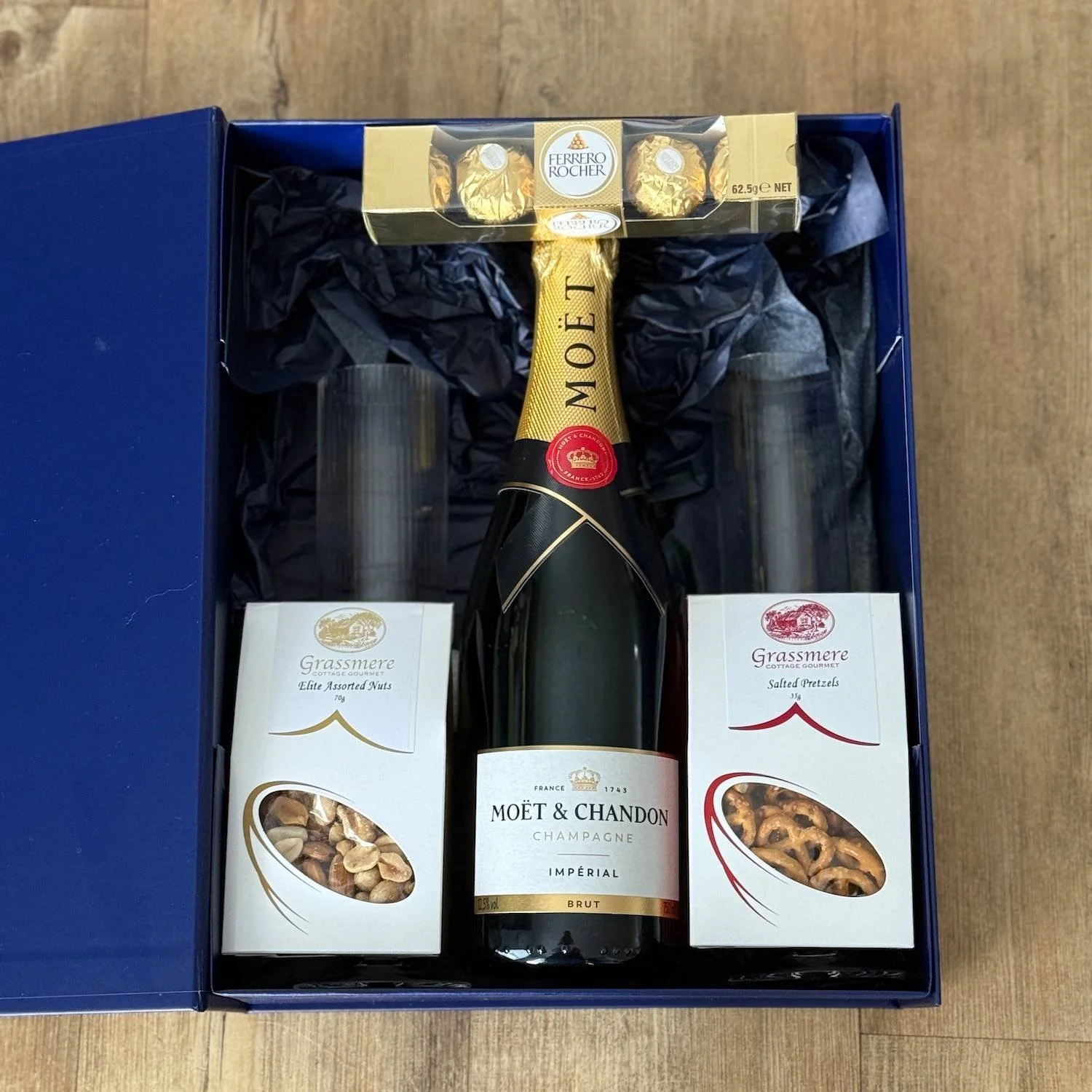 Gift box with bottle of Champagne, nuts, pretzels, chocolates and 2 champagne glasses.