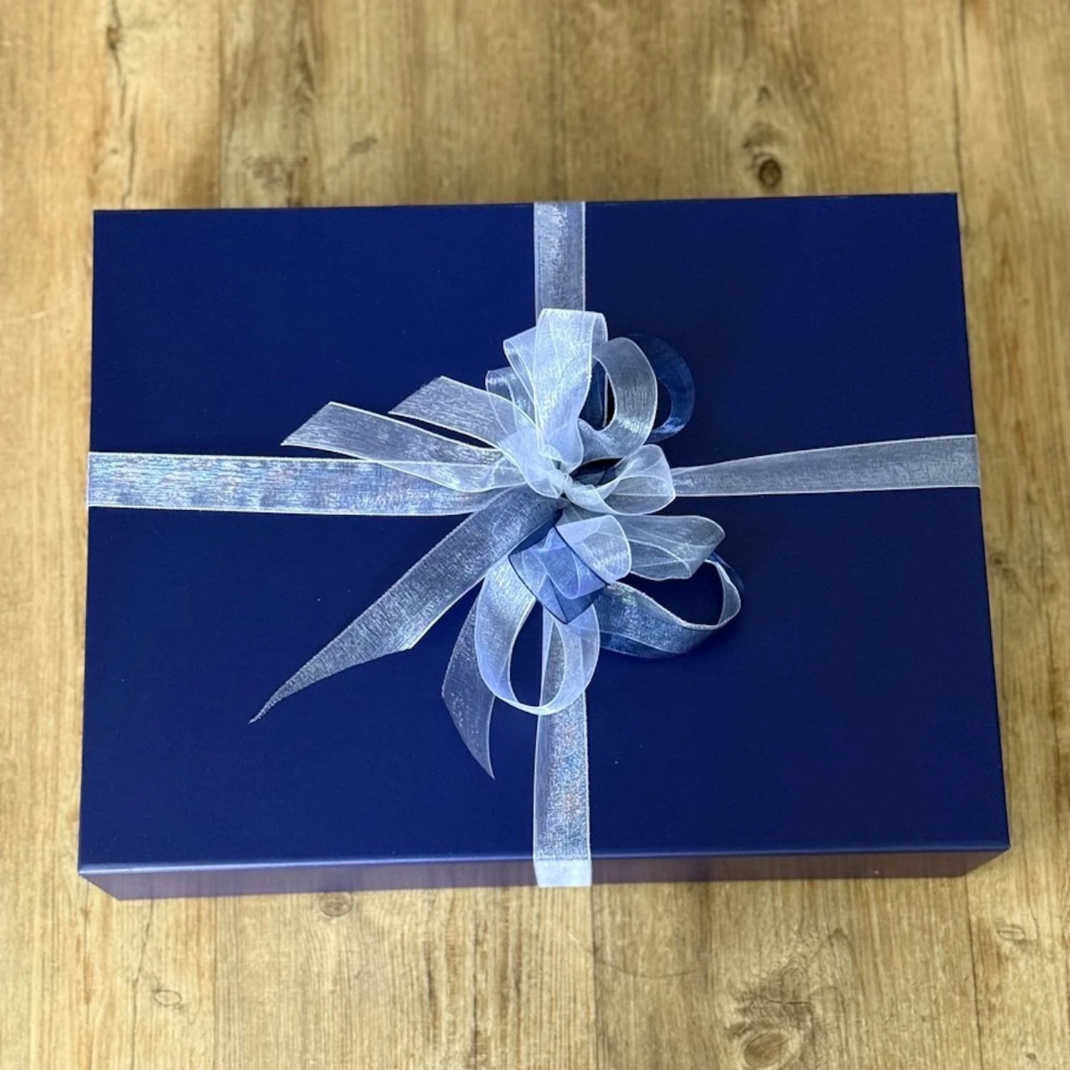 Blue Gift box tied with white blue and silver ribbon in a bow..