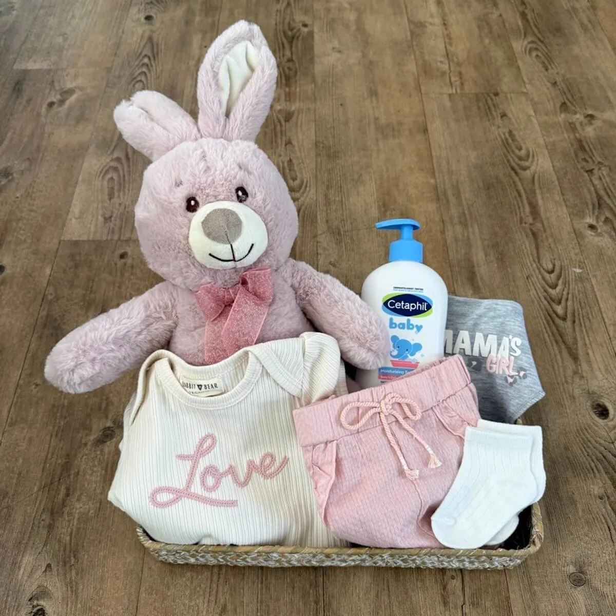 Hello Baby Girl gift basket with pink bunny, organic onesie and shorts, mama’s girl bib, socks and Cetaphil baby bath wash.