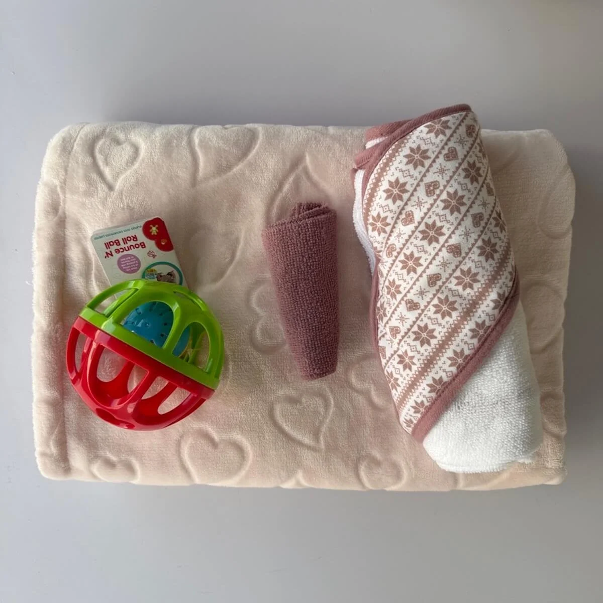 Pale pink blanket with a heart theme, hooded towel and washer and roll ball.