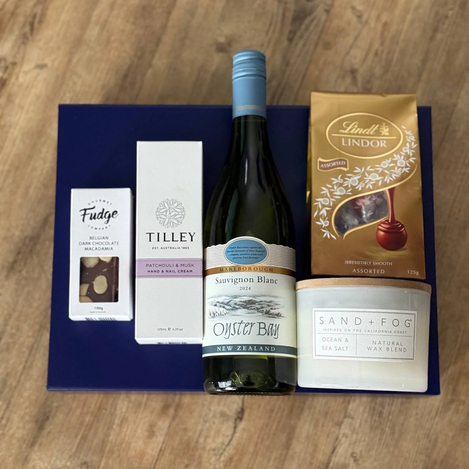 items sitting on blue gift box. Candle, chocolates, wine, hand cream and fudge.