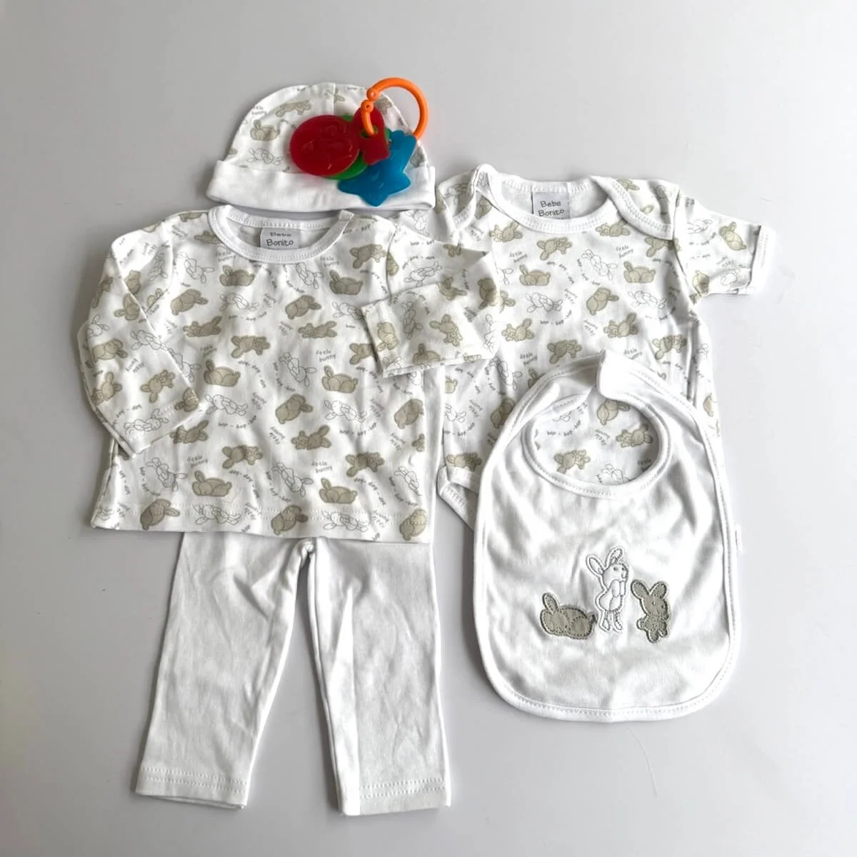 Five-piece baby clothing set with onesie, top, pants, bib, hat and baby rattle for a newborn girl