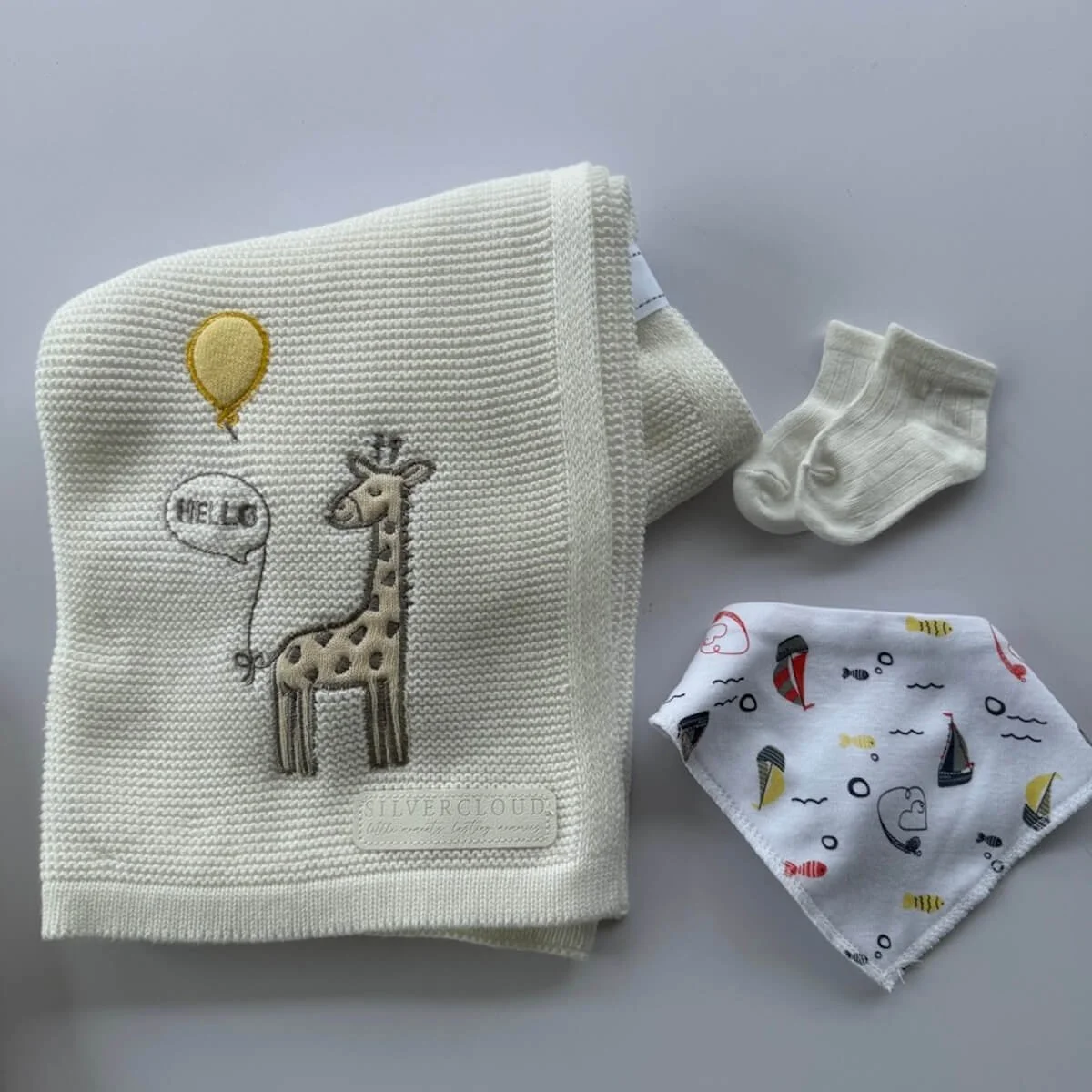 Baby blanket with giraffe theme, bandana bib and newborn baby socks displayed together as part of a baby boy gift basket.