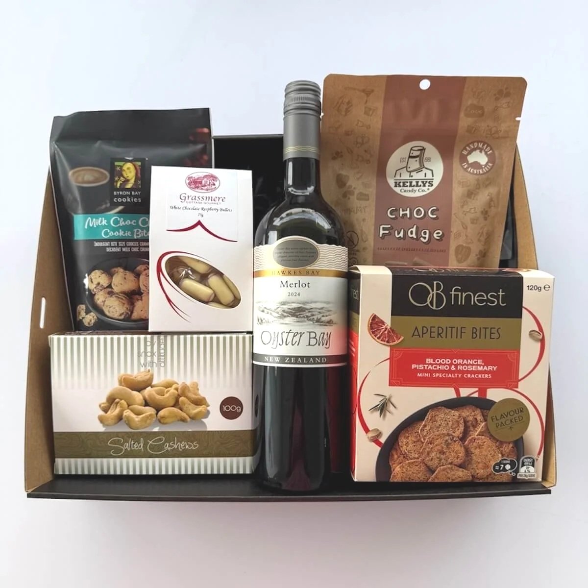 A gift basket containing a bottle of merlot wine, salted cashews, chocolate fudge, assorted crackers, and various snacks.