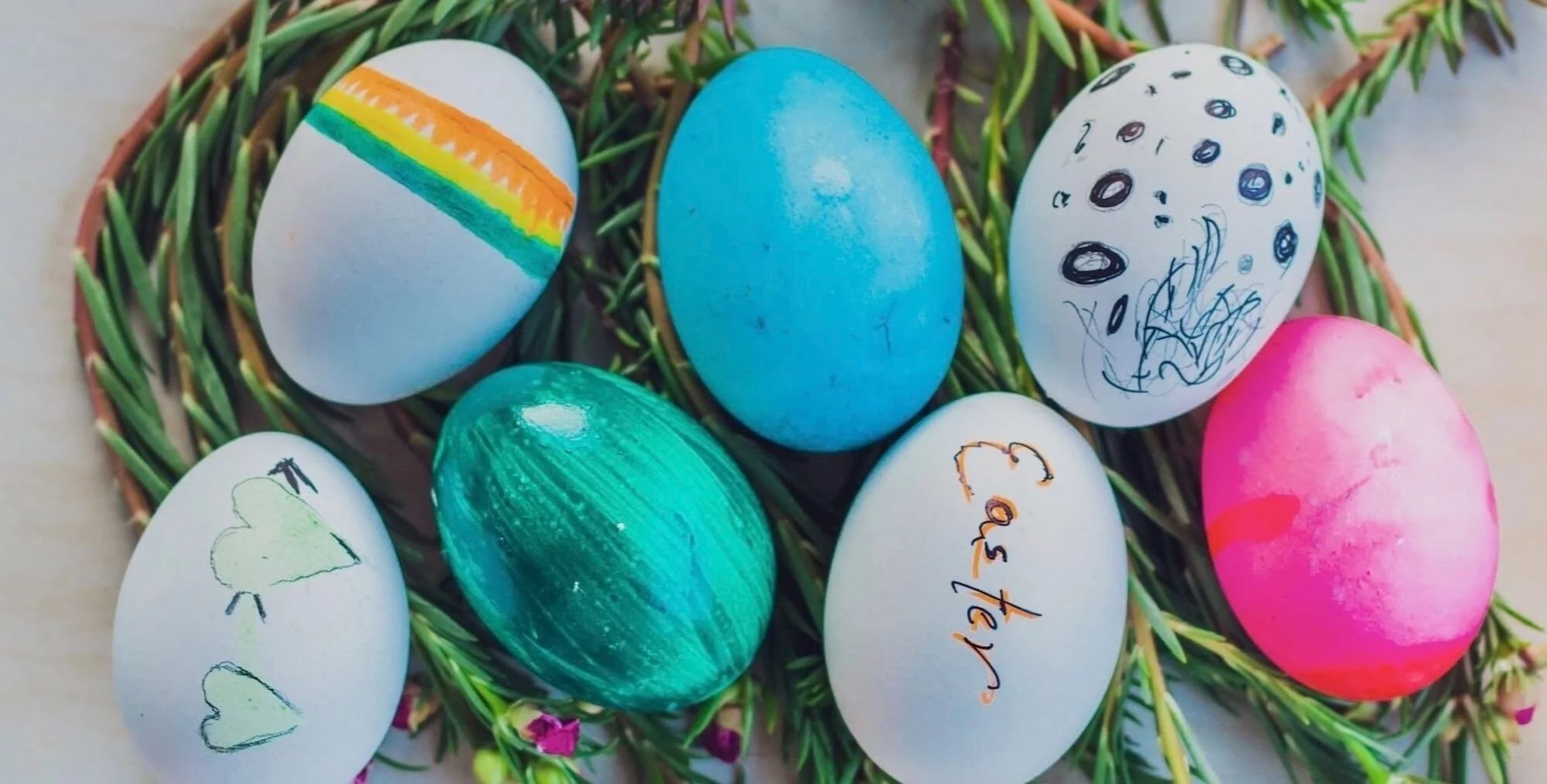Colorfully decorated Easter eggs in a basket with green foliage.