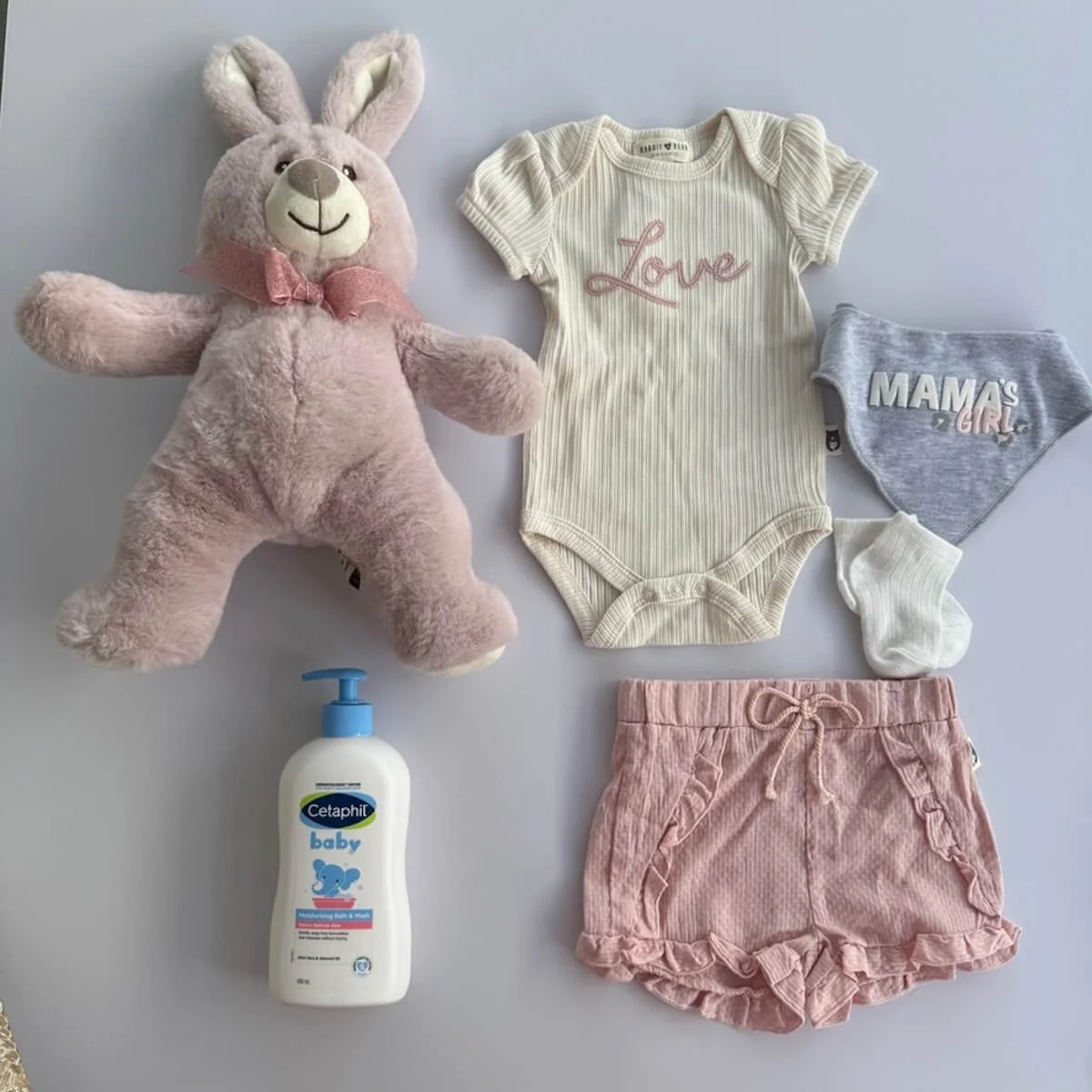 Baby girl clothing set with cream organic onesie embroidered Love, pink shorts, mama’s girl bib and white socks and bunny and baby wash included in hamper.