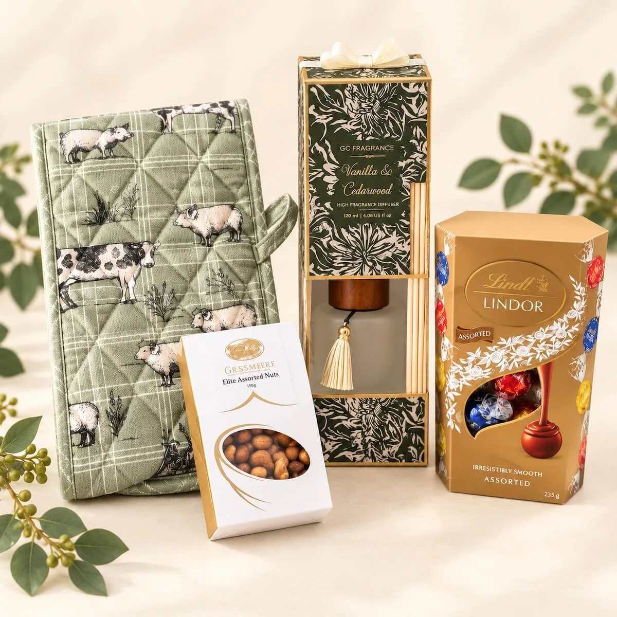 Housewarming gift selection featuring a sage green farmhouse oven mitt, Lindt Lindor chocolates, Grassmere nuts and Vanilla & Cedarwood diffuser.