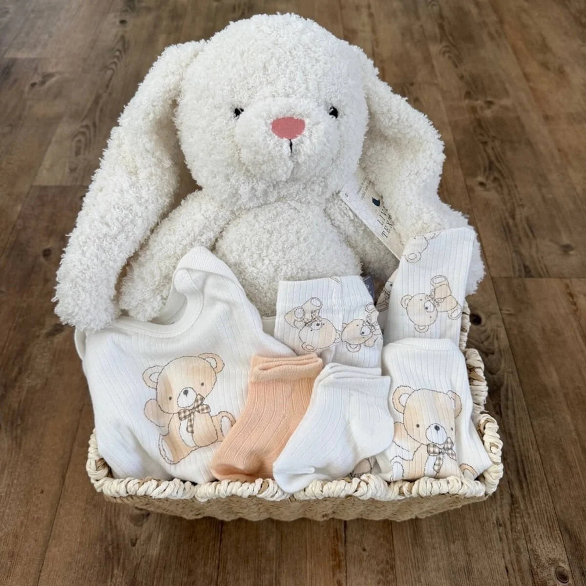 Baby gift hamper with plush white bunny and neutral baby outfit including long sleeve bodysuit, pants, hat, bib and socks in a woven basket