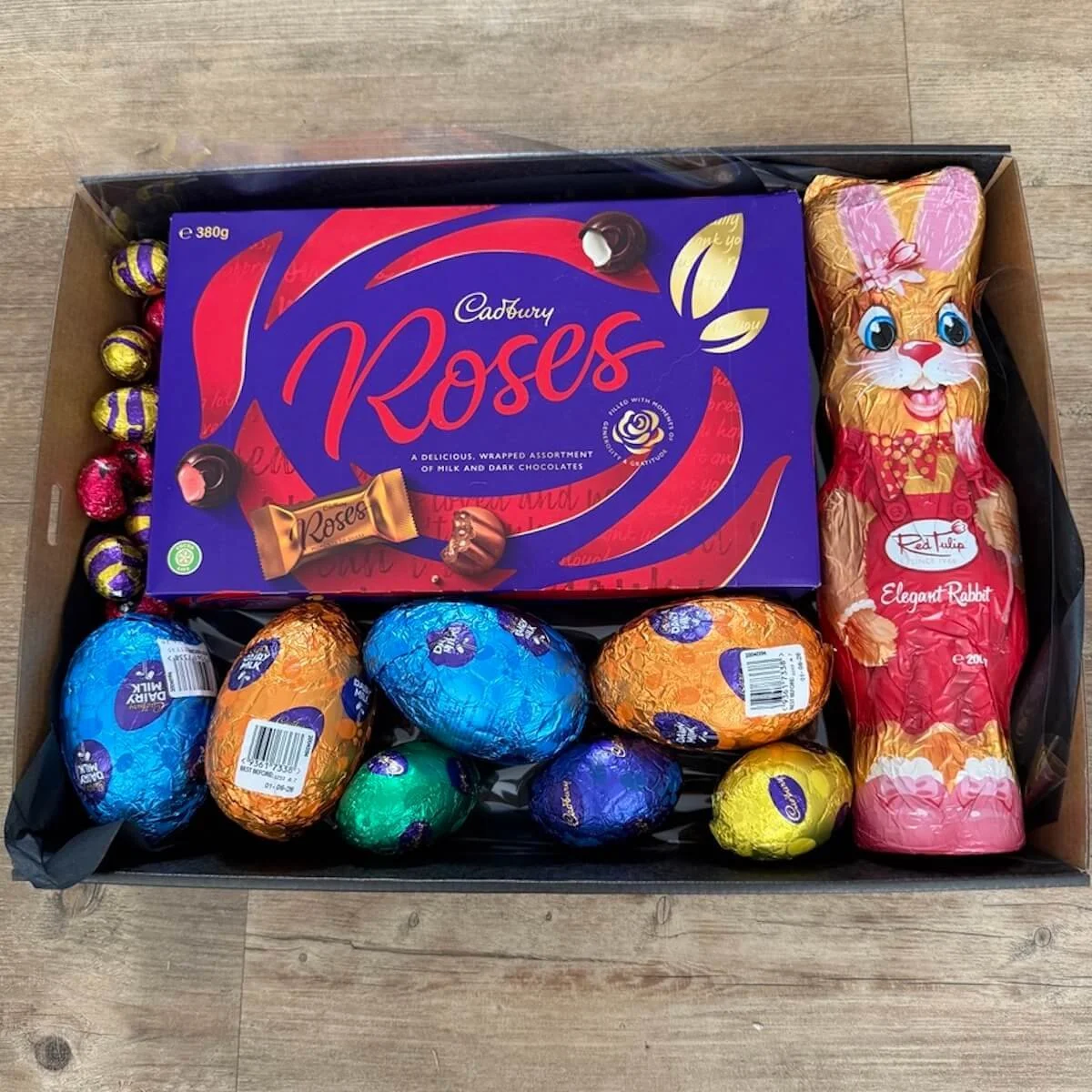 Open Easter Chocolate Gift Box with 380g Roses chocolates, chocolate Easter bunny and assorted Easter eggs in a black tray.