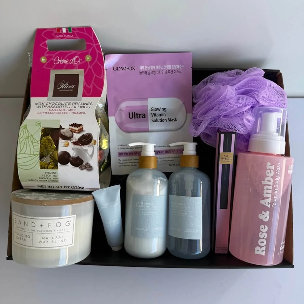 Sand and Fog gift hamper with body products and a sand and fog candle. Includes a face mask, chocolates and washer with purse perfume.