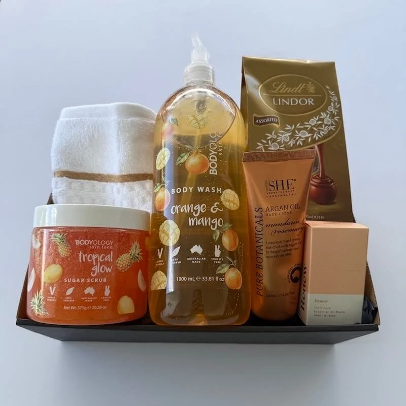 A womans gift hamper with Australian pamper items. Body wash, body scrub, chcolates, hand cream, chocolates and a wash cloth.