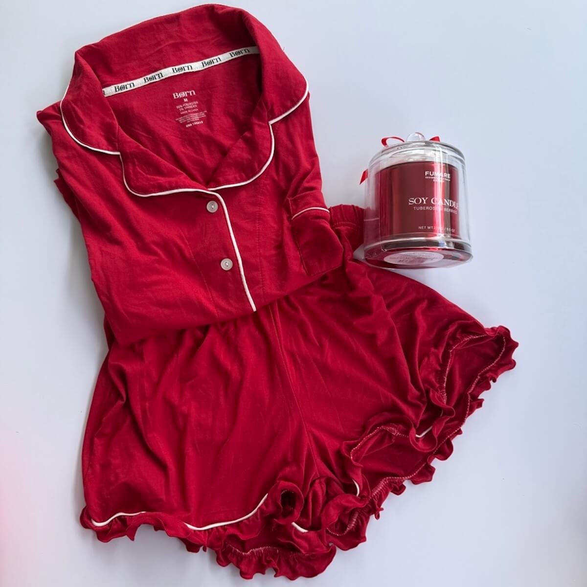 Women's short sleeve red pajama set featuring white cord piping and contrasting white buttons displayed with red candle.