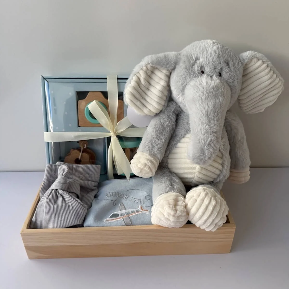 Baby gift tray with a toy elephant and a 3 piece clothing set and a 3 piece rattle toy set.