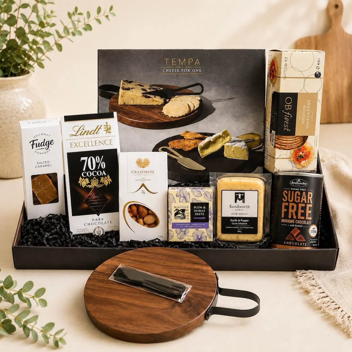Gourmet cheese hamper with Tempa Cheese for One board, cheddar, crackers, nuts, dark chocolate, fudge and drinking chocolate displayed on a natural kitchen bench.