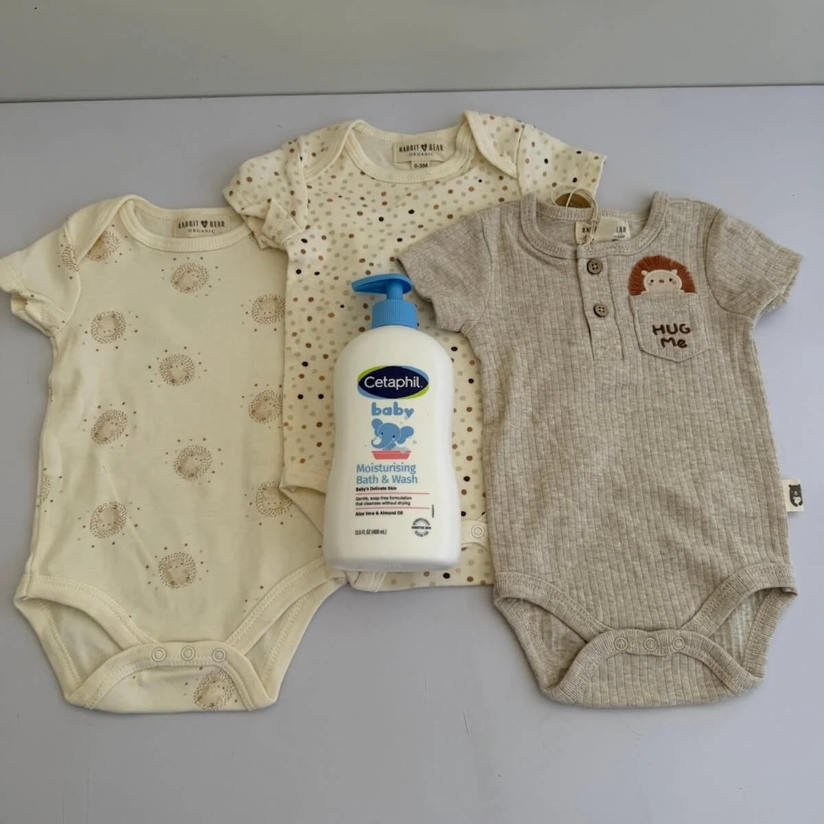 Three soft organic cotton baby bodysuits in neutral colours, size 0–3 months. Comfortable everyday essentials for newborn babies.