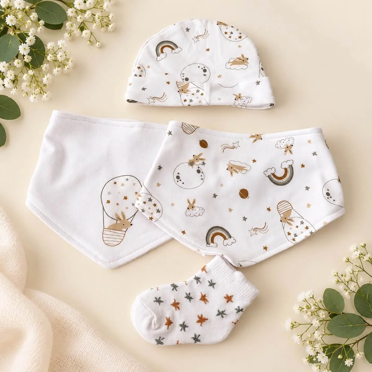 Matching baby hat, two bandana bibs and star-patterned socks in soft neutral colours with bunny and rainbow prints.