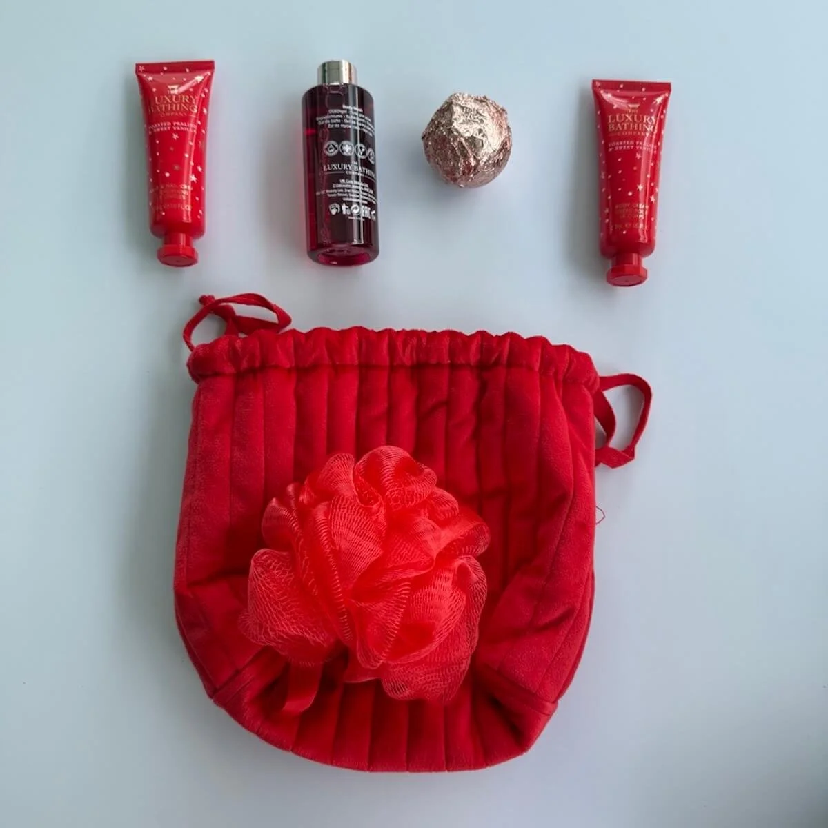Pack of luxury pamper products for the Bed and Bubbles Hamper, including hand cream, body wash, bath bomb, body cream, and mesh washer