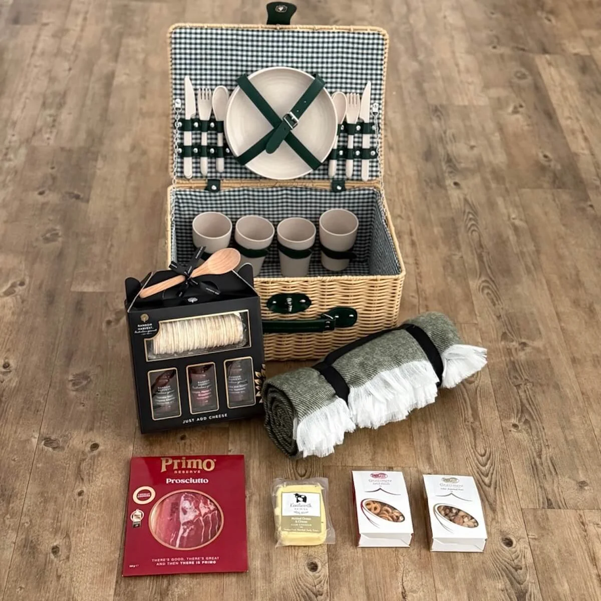 Gourmet picnic hamper for four with plastic wicker basket, picnic blanket, plates, cutlery, cups, cheese, prosciutto, nuts, chutneys, and crackers