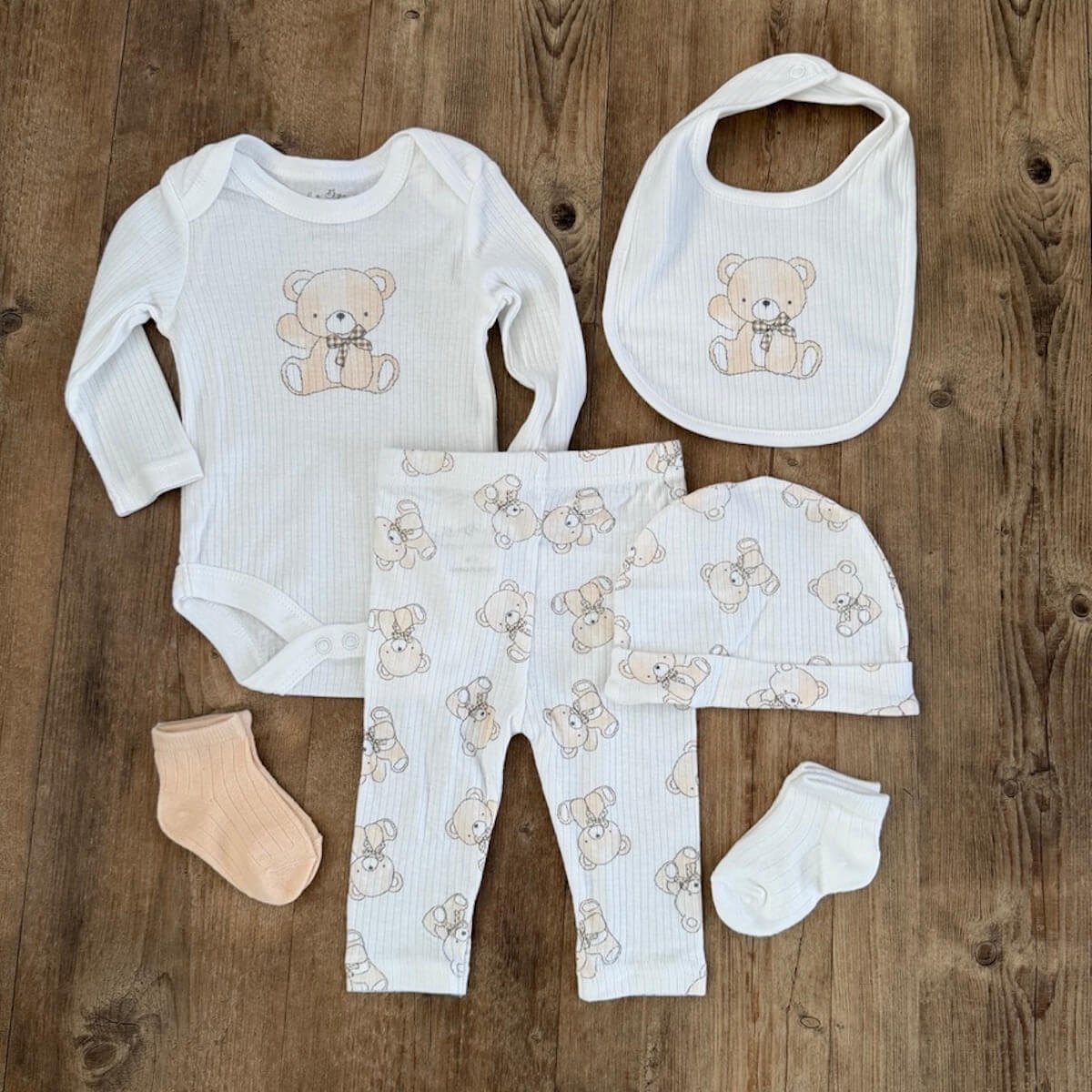 Neutral baby clothing set with long sleeve legless bodysuit, matching pants, hat, bib and two pairs of socks with teddy print