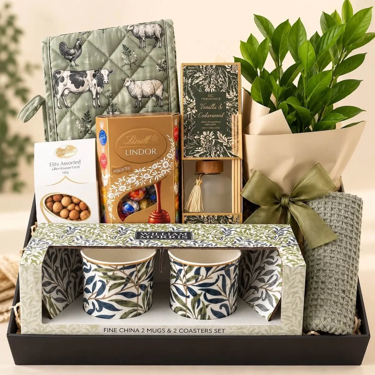 Luxury housewarming gift hamper with Zanzibar plant, farmhouse oven mitt, William Morris mugs, Lindt chocolates and home fragrance diffuser.