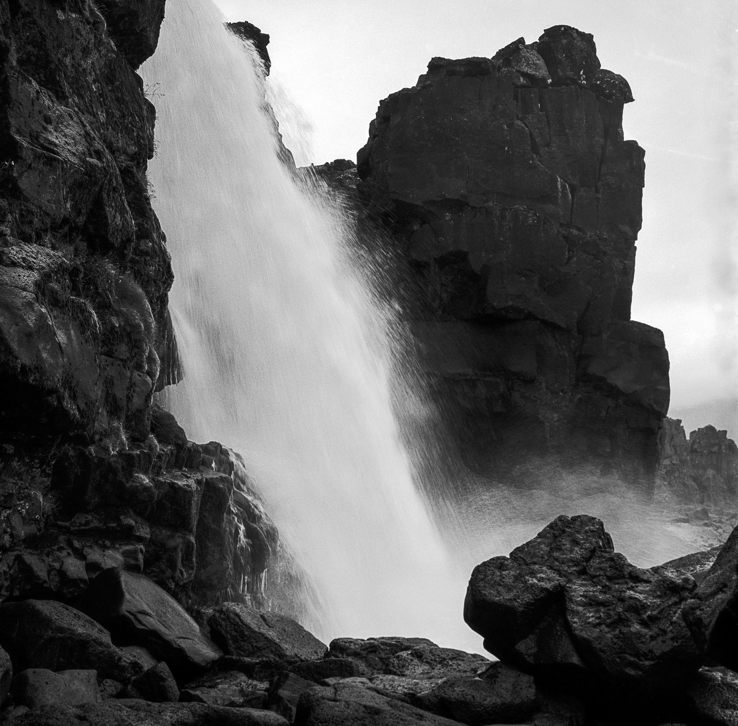 Black and white photo of a waterfall cascading over rocks with large boulders in the foreground.
