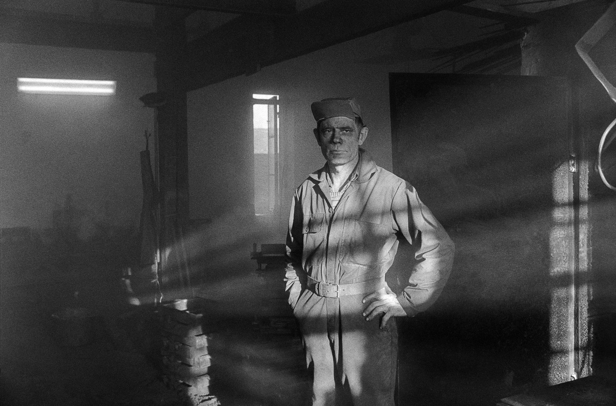 Black and white photo of man in a military uniform standing in a room with his hand on his hip, with sunlight streaming through a window and frosted beams of light across the image.