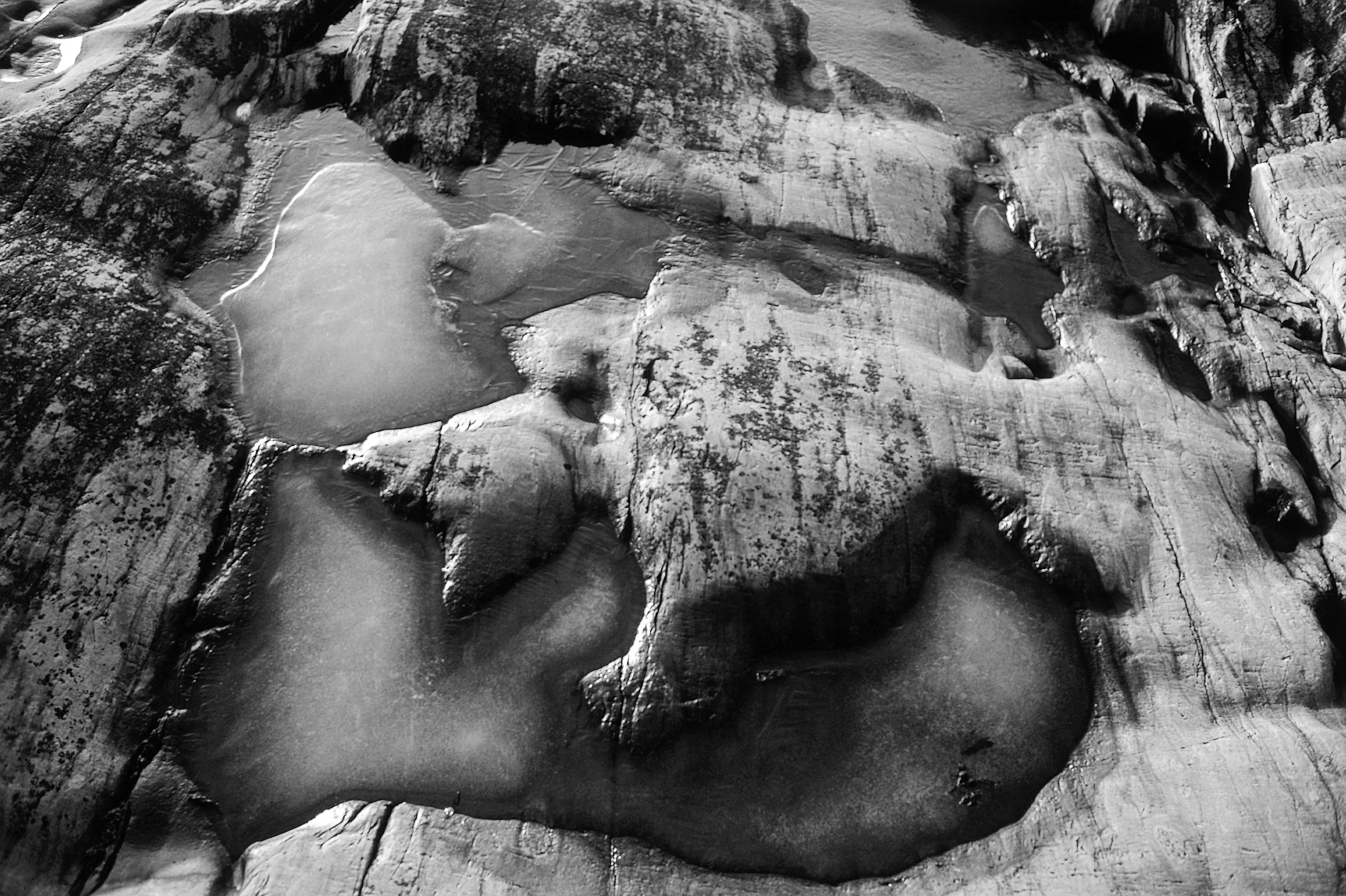 Black and white photo of ice formations and water pools on a rugged rocky surface.