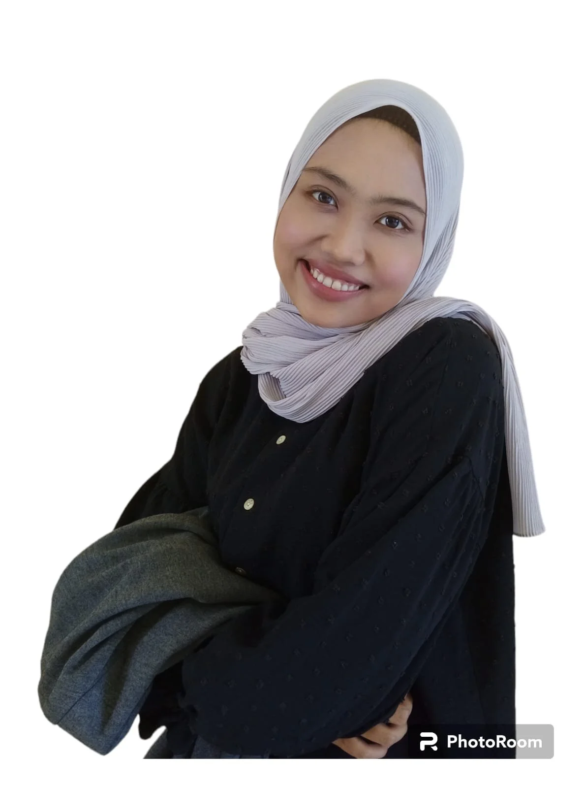 Smiling woman wearing a white hijab and a black top, holding a gray coat, against a white background.