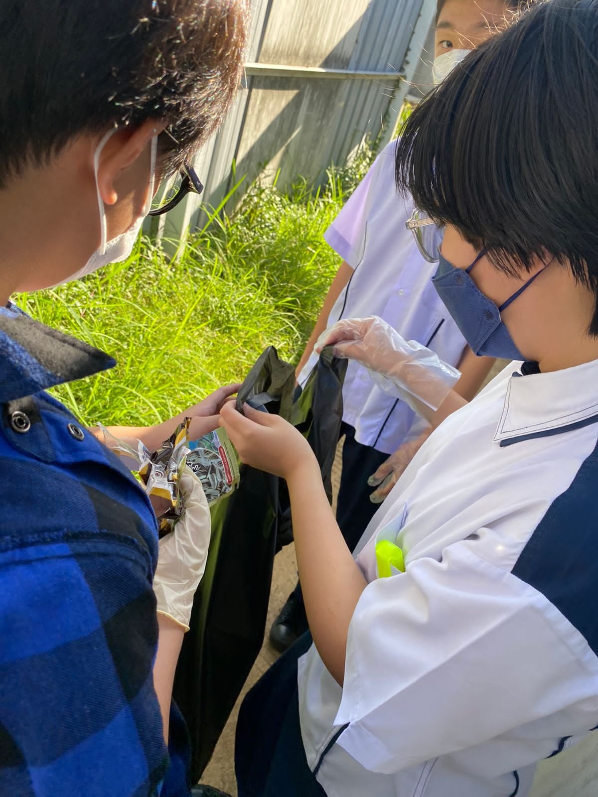 Group of students examining items in a plastic bag outdoors, wearing masks and gloves.