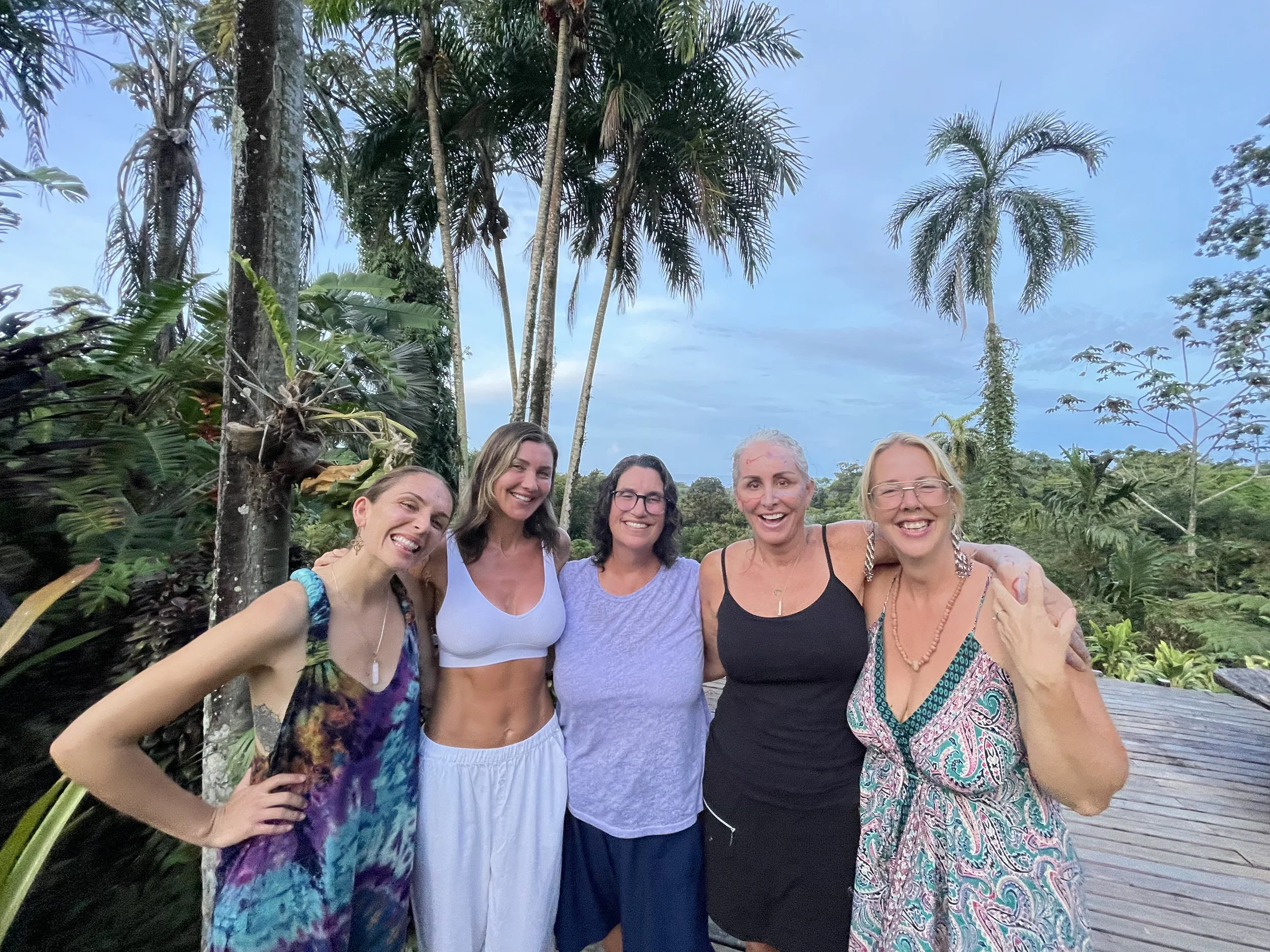 group of women standing together, smiling, palm trees in the background, blue sky