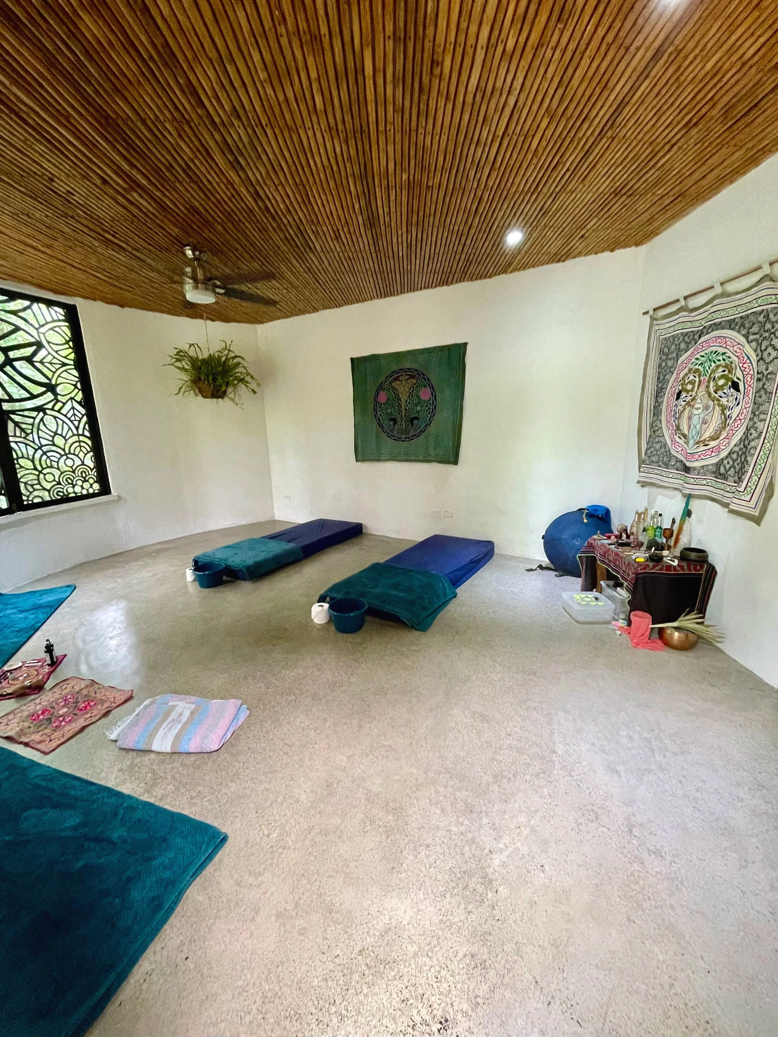 A room with a wooden ceiling, cream walls and colourful tapestries hung up, with blue mats on  floor