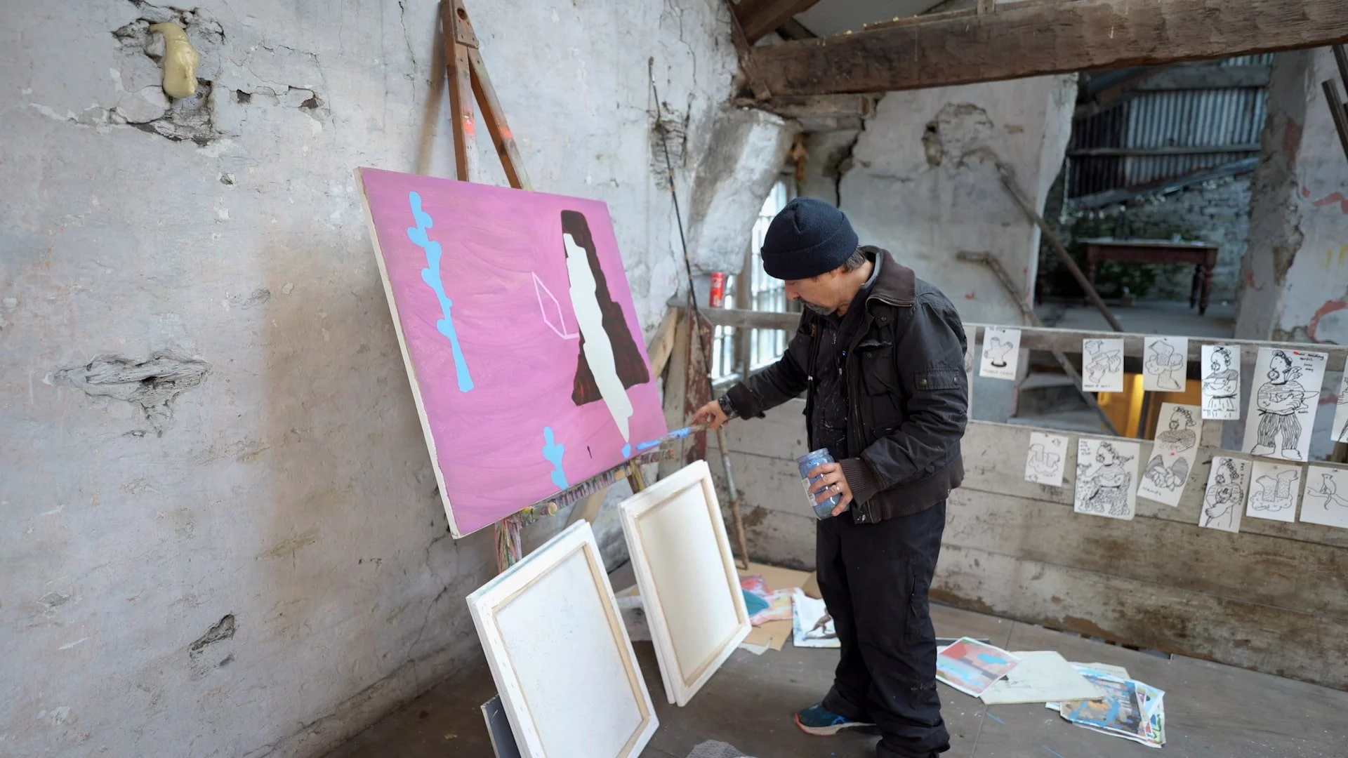Irish artist Martin Finnin painting blue forms onto pink abstract canvas on easel in West Cork studio, early stage oil painting with dark brown and cream shapes emerging, painting in progress