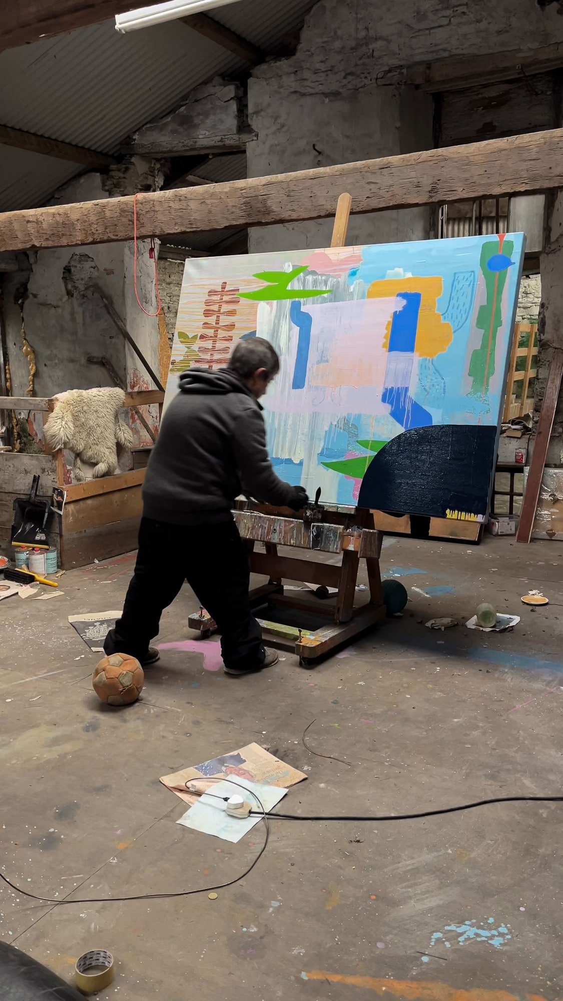 Irish artist working on large abstract oil painting on easel in West Cork studio, blue green orange and dark navy forms, old football and found objects on studio floor, Martin Finnin