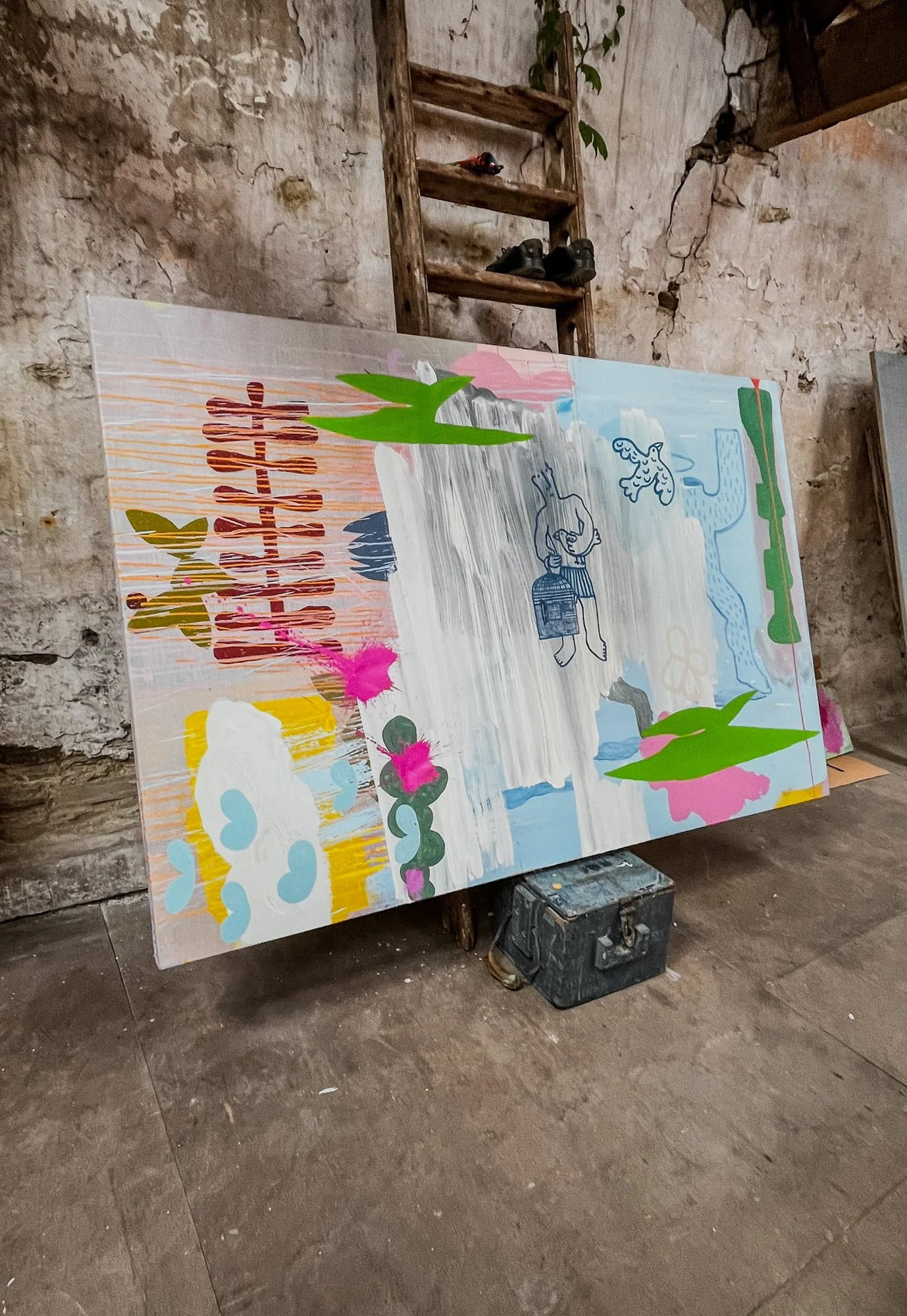 Large abstract oil painting leaning against stone wall in West Cork studio, blue green pink and white forms with small drawn figures emerging, old ladder and bronze sculptures in background, Martin Finnin Irish artist