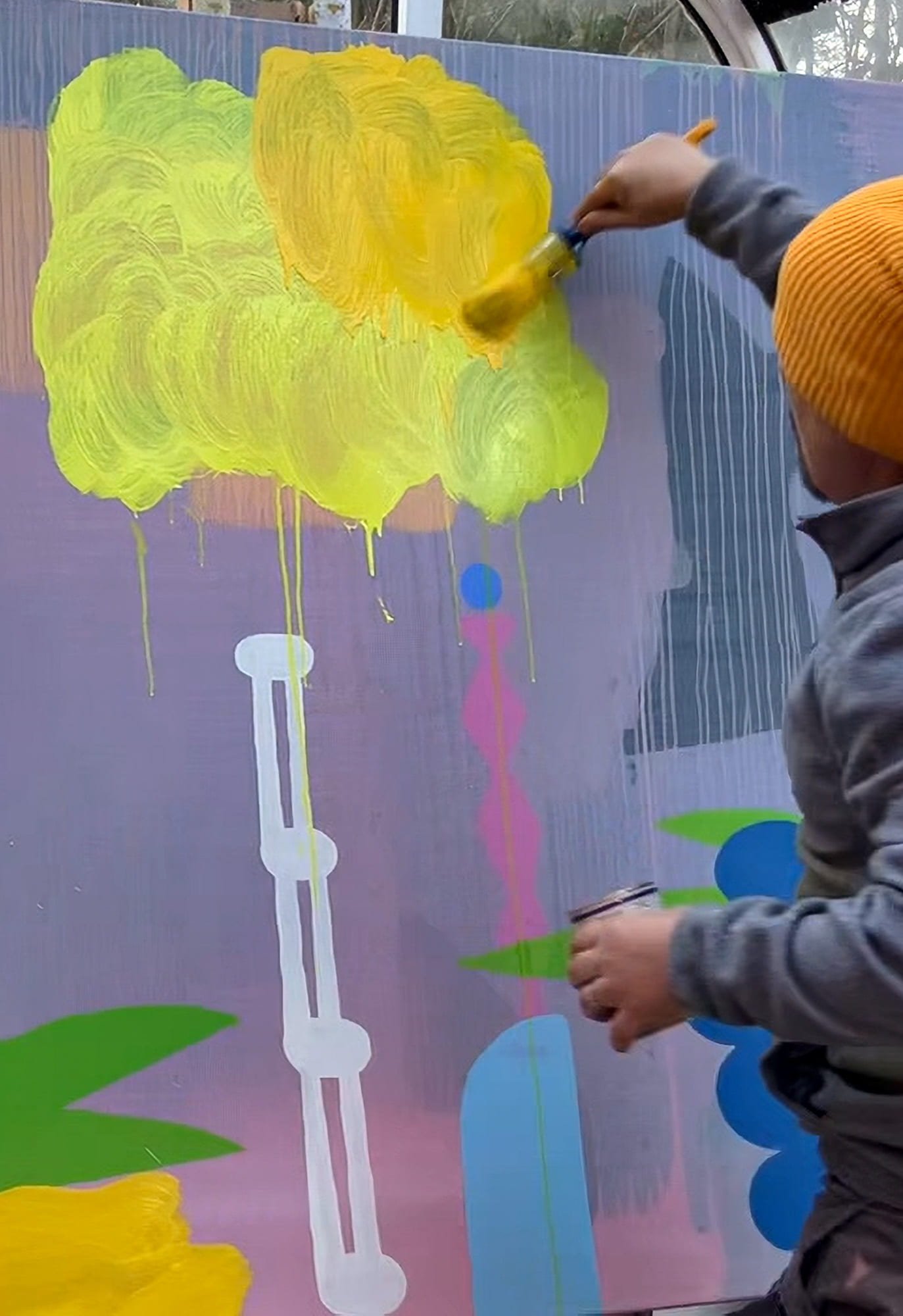 Irish artist painting vivid yellow cloud form onto large canvas outdoors, green blue pink and white forms visible below, abstract oil painting nearing completion, Martin Finnin West Cork