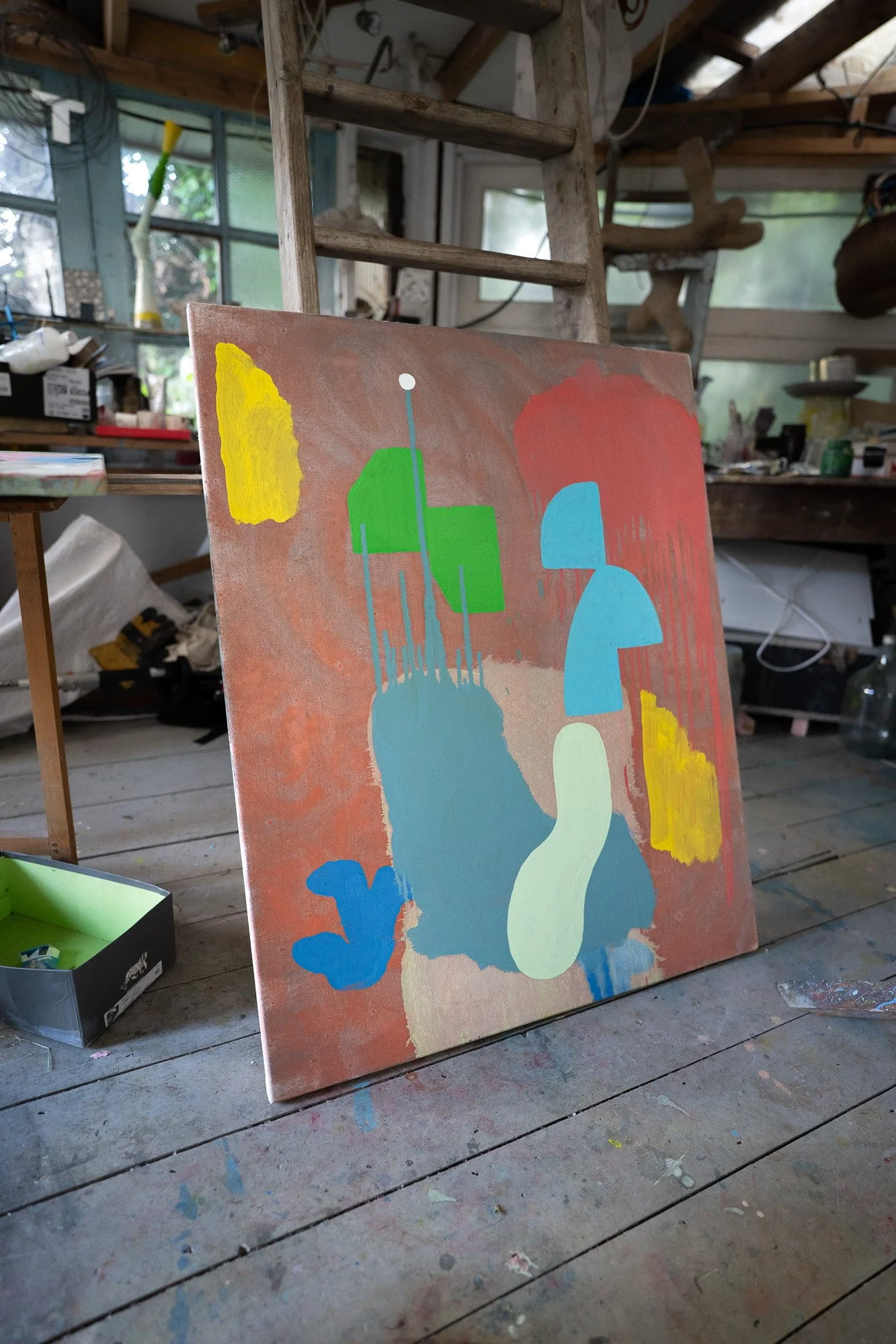 Abstract oil painting in progress leaning against studio wall, terracotta ground with yellow green blue and red forms, West Cork studio interior, Martin Finnin Irish artist