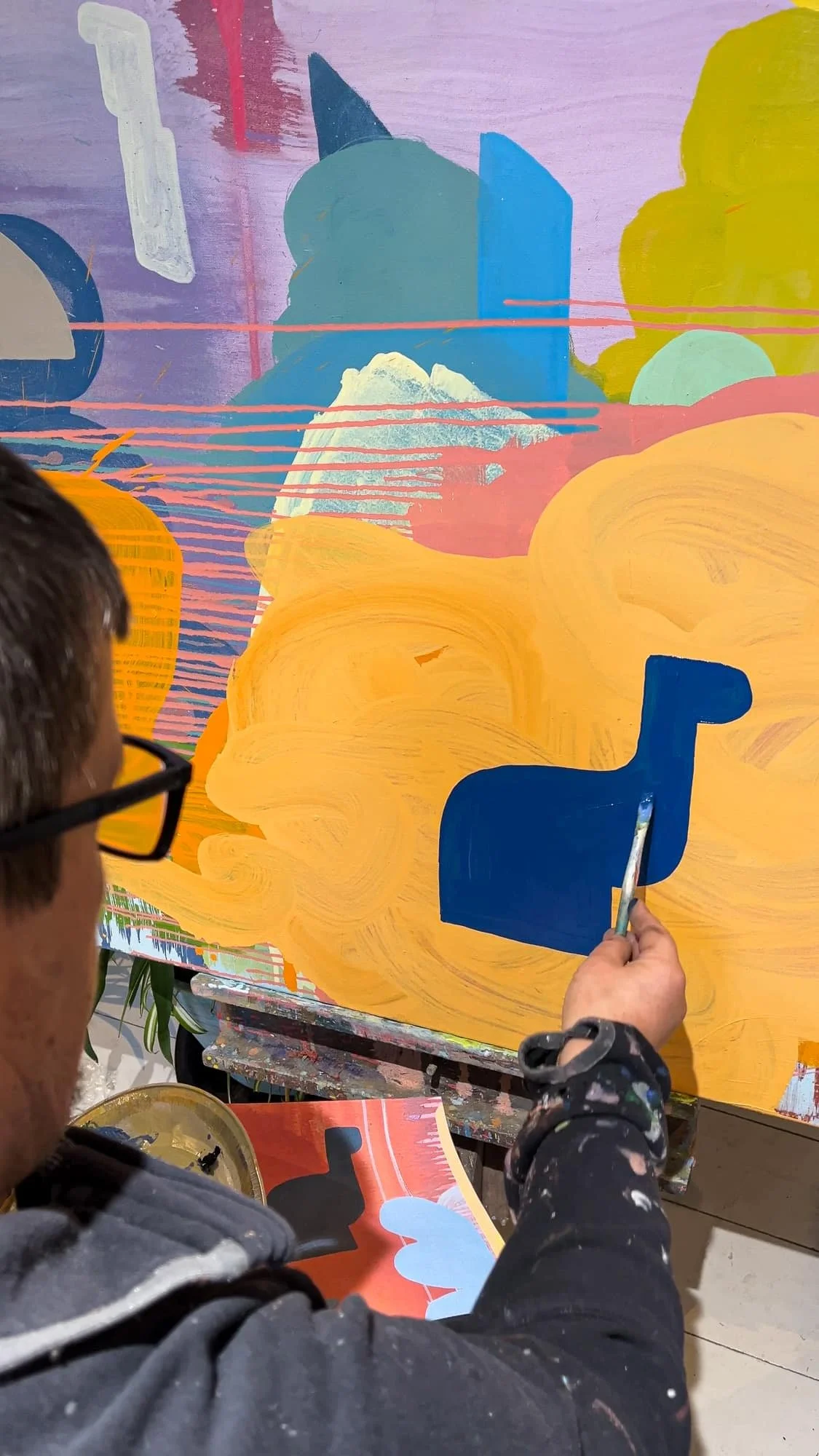 Irish artist Martin Finnin painting bold blue form onto large abstract canvas, vivid orange yellow and teal oil painting in progress, close up of artist working in studio