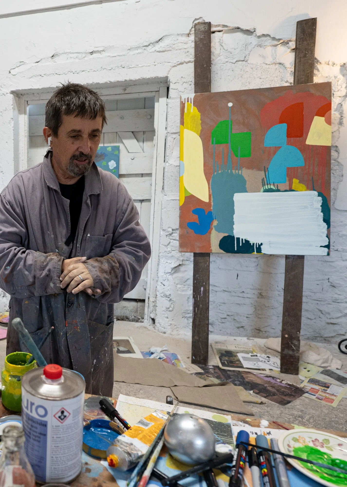 Irish artist in paint-covered coat standing beside abstract oil painting in progress on easel, Ballyfin House studio with brushes and materials in foreground, Martin Finnin