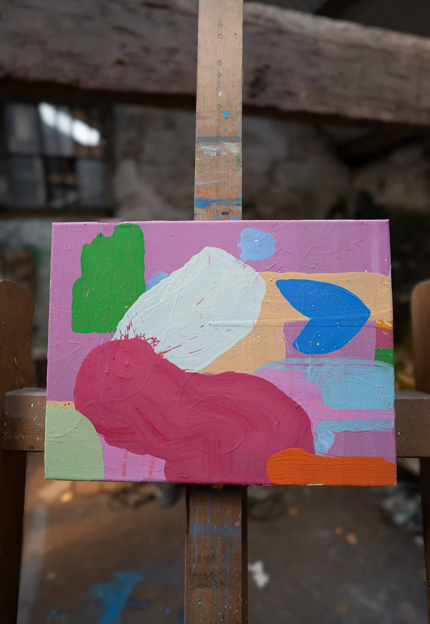 Abstract oil painting near completion on easel in West Cork studio, vivid pink crimson green white blue and orange forms, stone-walled studio blurred in background, Martin Finnin Irish artist