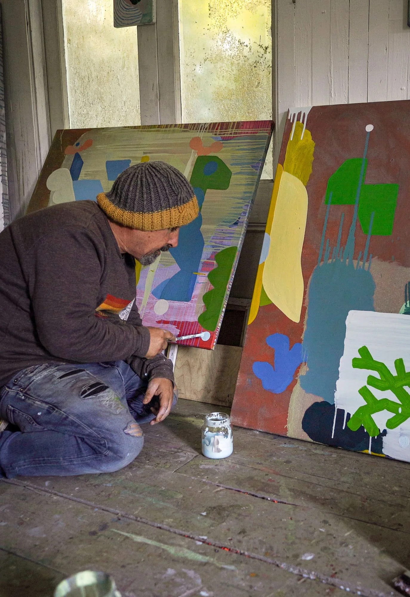 Irish artist working close to canvas on studio floor surrounded by multiple paintings in progress, blue green yellow and terracotta forms, West Cork studio, Martin Finnin