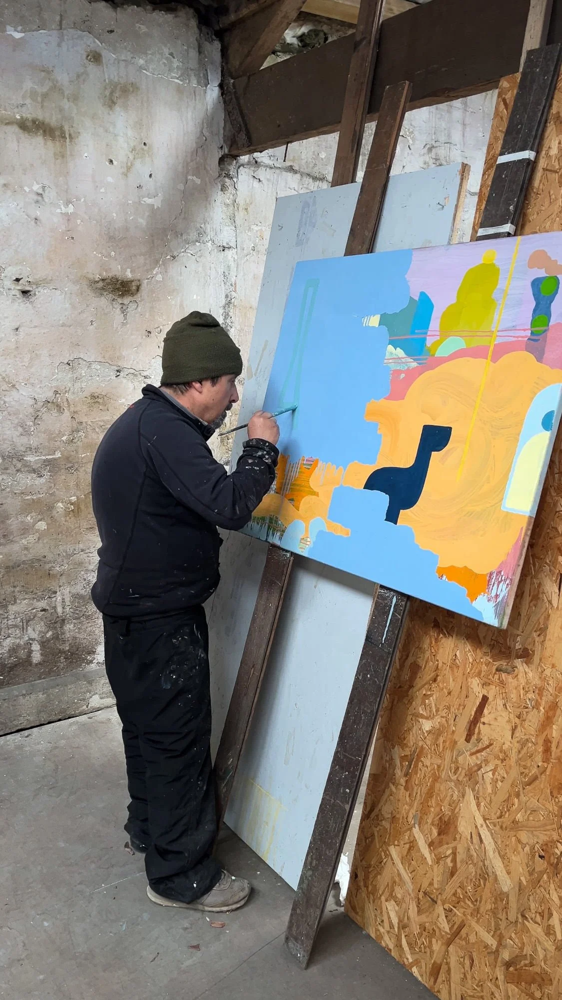 Irish artist Martin Finnin adding final detail to large abstract oil painting leaning against stone wall, blue orange and yellow canvas in final stage, West Cork studio, Martin Finnin Irish artist