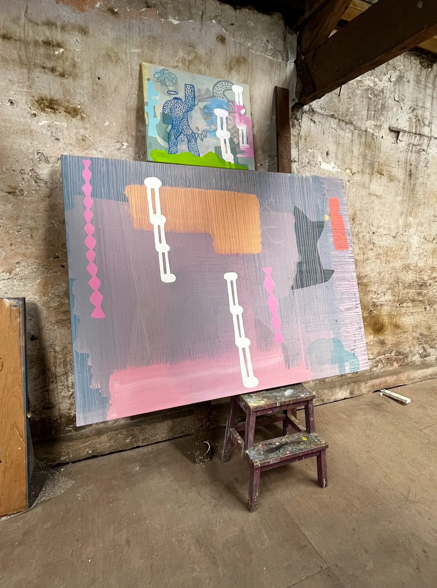 Large abstract oil painting in progress leaning against stone wall in West Cork studio, lavender pink orange and white forms developing, smaller figurative painting visible above, Martin Finnin Irish artist