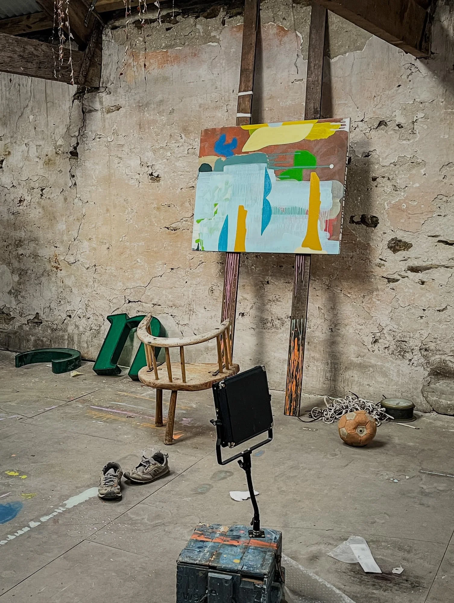 Abstract oil painting on easel in West Cork studio, terracotta yellow blue and green forms, found objects on floor including green letters and football, Martin Finnin Irish artist